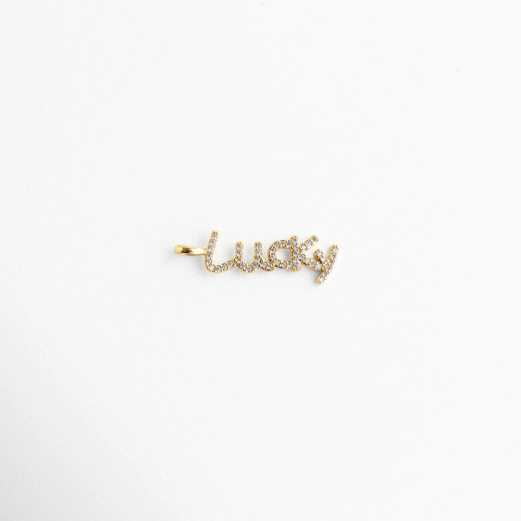 Dije lucky dorado con zirconias detalle pequeño brillante, Colgante lucky con incrustaciones de zirconia vista cercana, Detalle de dije lucky con acabado dorado y piedras brillantes, Colgante pequeño lucky con zirconias diseño fino, Dije tipografía lucky con brillo tipo diamante zirconia
