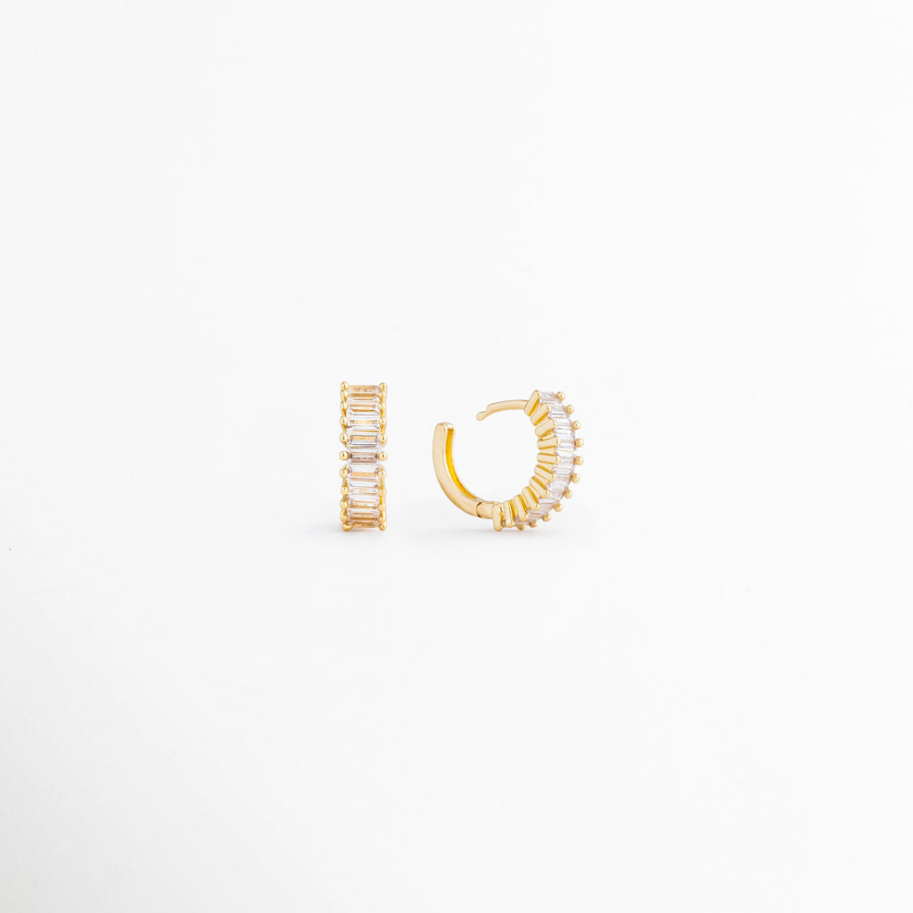 Isabel Golden Hoops desde ángulo lateral mostrando sus zirconias brillantes, Detalle de arracadas doradas pequeñas con acabado en Oro 18K, Vista angular de hoops elegantes y versátiles para mujer, Aretes dorados con zirconias y diseño clásico contemporáneo, Detalle de arracadas compactas ideales para looks diarios.