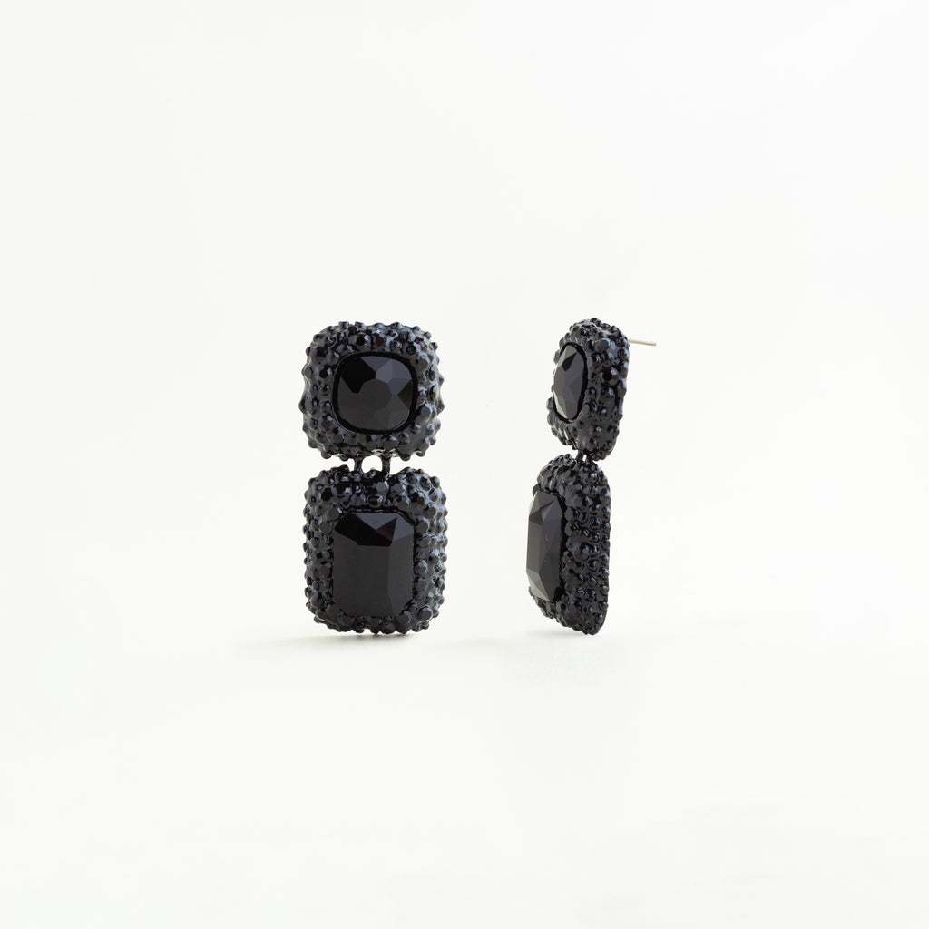 Vista lateral de aretes negros geométricos con cristales A5 y acabado brillante, Perfil de pendientes largos negros con diseño rectangular y detalles de cristales, Aretes colgantes negros vistos de lado con estructura elegante y moderna, Detalle lateral de aretes de cobre enchapado con cristales negros brillantes, Pendientes geométricos negros con diseño sofisticado y acabado de lujo vistos de perfil.