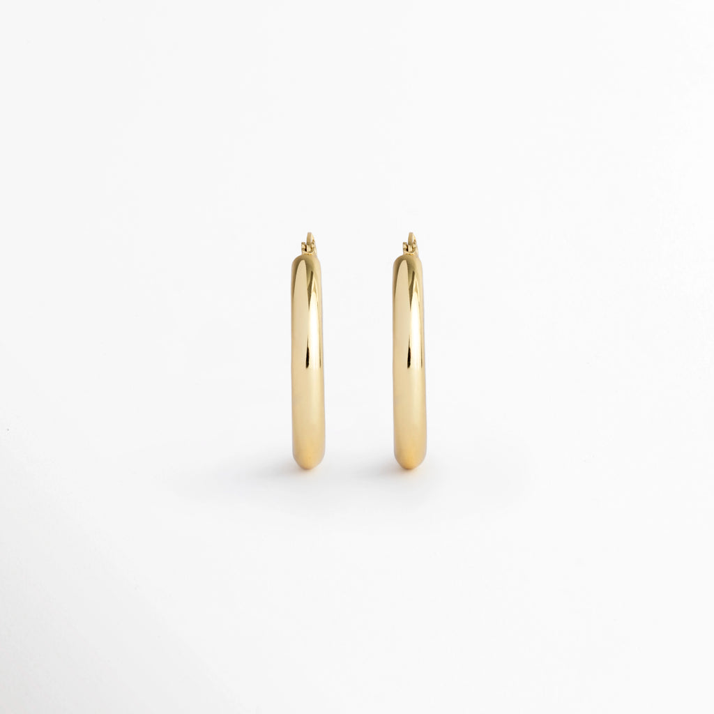 Aretes Lumi Small de silueta tubular de arracada clásica en enchapado de oro 18K con acabado pulido, vista frontal de par sobre fondo blanco, Vista de frente de arracadas doradas de tamaño mediano (2.5 cm) de perfil redondeado liso sobre superficie clara, Par de aros/arracadas doradas tubulares de volumen medio con pulido de alto brillo espejo, Aretes estilo arracada chunky lisas enchapadas en oro 18K de 2.5 cm de diámetro.