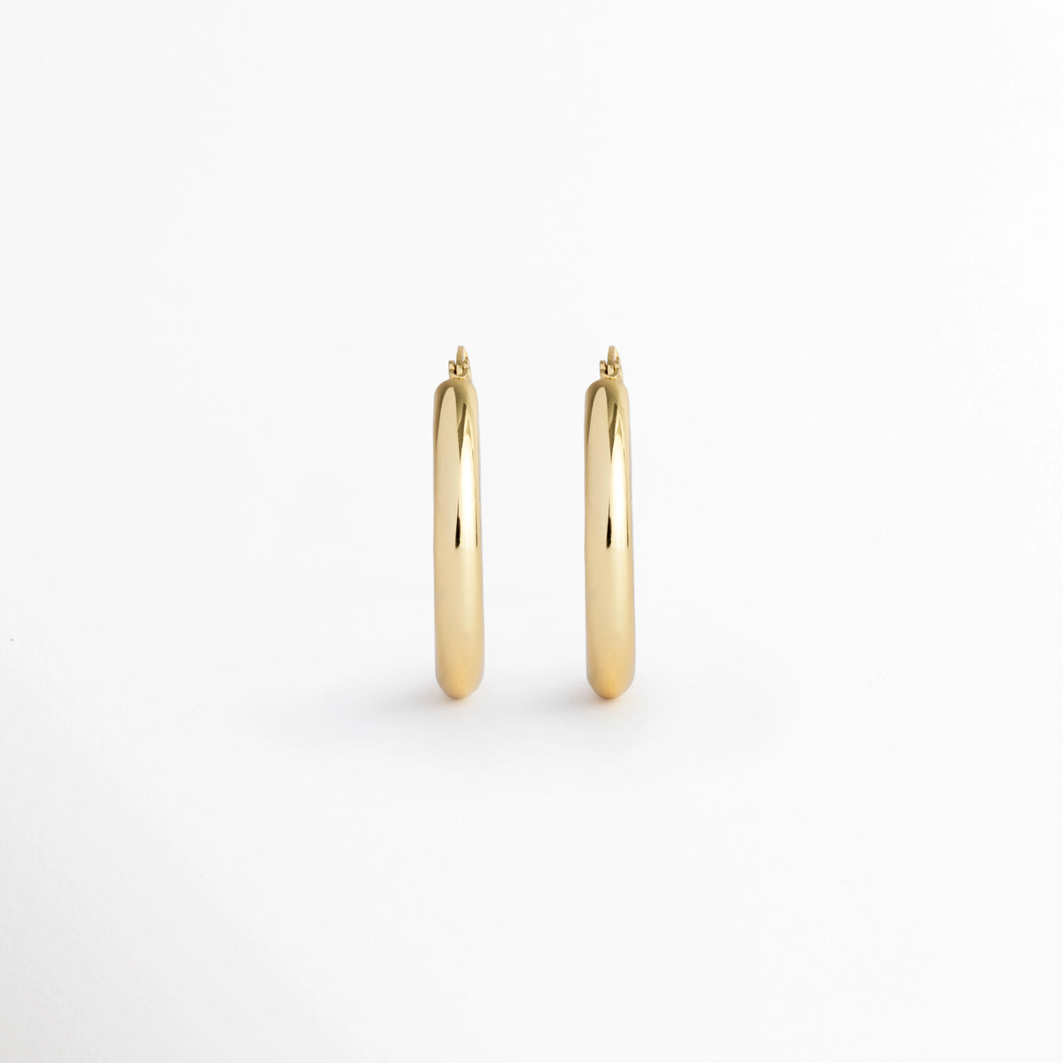Aretes Lumi Small de silueta tubular de arracada clásica en enchapado de oro 18K con acabado pulido, vista frontal de par sobre fondo blanco, Vista de frente de arracadas doradas de tamaño mediano (2.5 cm) de perfil redondeado liso sobre superficie clara, Par de aros/arracadas doradas tubulares de volumen medio con pulido de alto brillo espejo, Aretes estilo arracada chunky lisas enchapadas en oro 18K de 2.5 cm de diámetro.