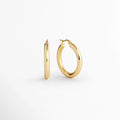 Aretes Lumi Small vistos de perfil y tres cuartos mostrando el grosor del tubo y la curvatura del aro, Vista en ángulo de arracadas doradas enchapadas en oro 18K mostrando la solidez de la forma circular de 2.5 cm, Acercamiento a la silueta limpia y redondeada del aro Lumi Small en acabado espejo sobre fondo neutro, Detalle del diámetro de 2.5 cm de arracada dorada pulida en toma de tres cuartos.