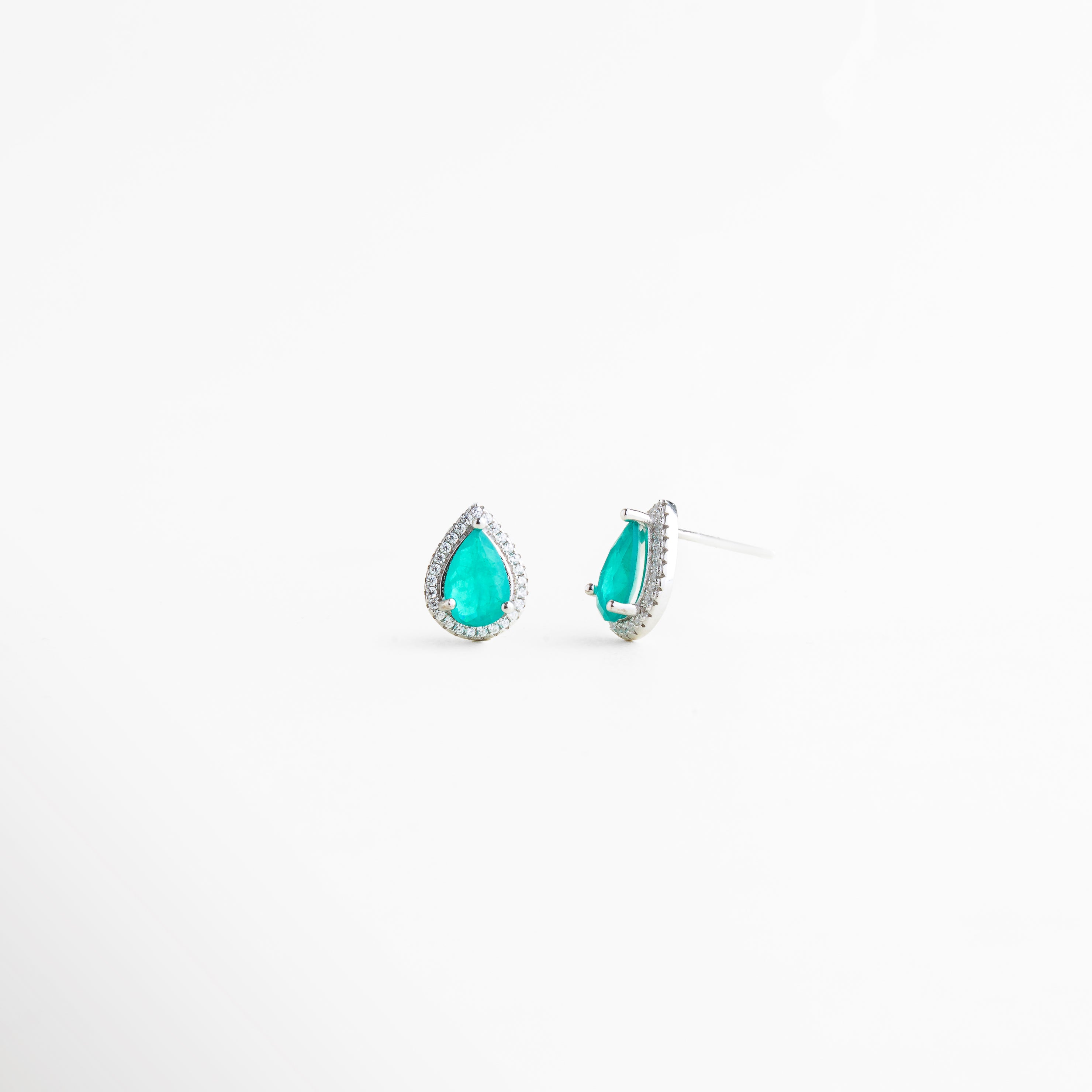 Vista lateral de aretes tipo lágrima en plata con piedra turquesa brillante, Perfil de pendientes pequeños con diseño elegante y acabado en plata enchapada, Aretes de plata 925 con cristales sintéticos vistos de lado sobre fondo blanco, Detalle lateral de pendientes tipo gota con brillo sofisticado y diseño minimalista, Aretes delicados con piedra turquesa y estructura de plata vistos de perfil.