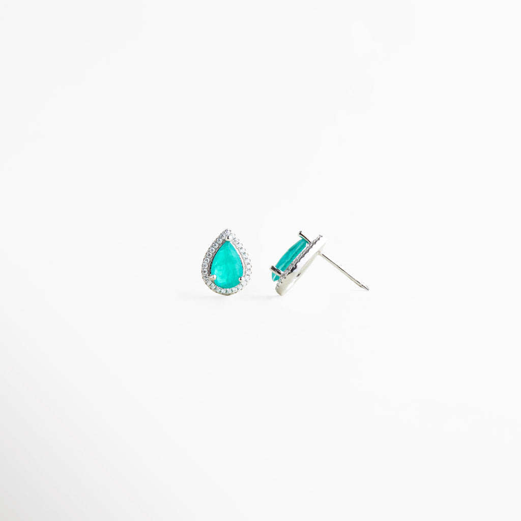Aretes de plata ley 925 con broche tipo poste y piedra turquesa brillante, Vista inclinada de pendientes tipo gota con incrustaciones brillantes y acabado elegante, Detalle de aretes pequeños en plata con diseño sofisticado y cristales sintéticos, Pendientes de lágrima color turquesa con estructura fina y acabado brillante, Aretes minimalistas de plata con piedra azul turquesa y cierre clásico de poste.