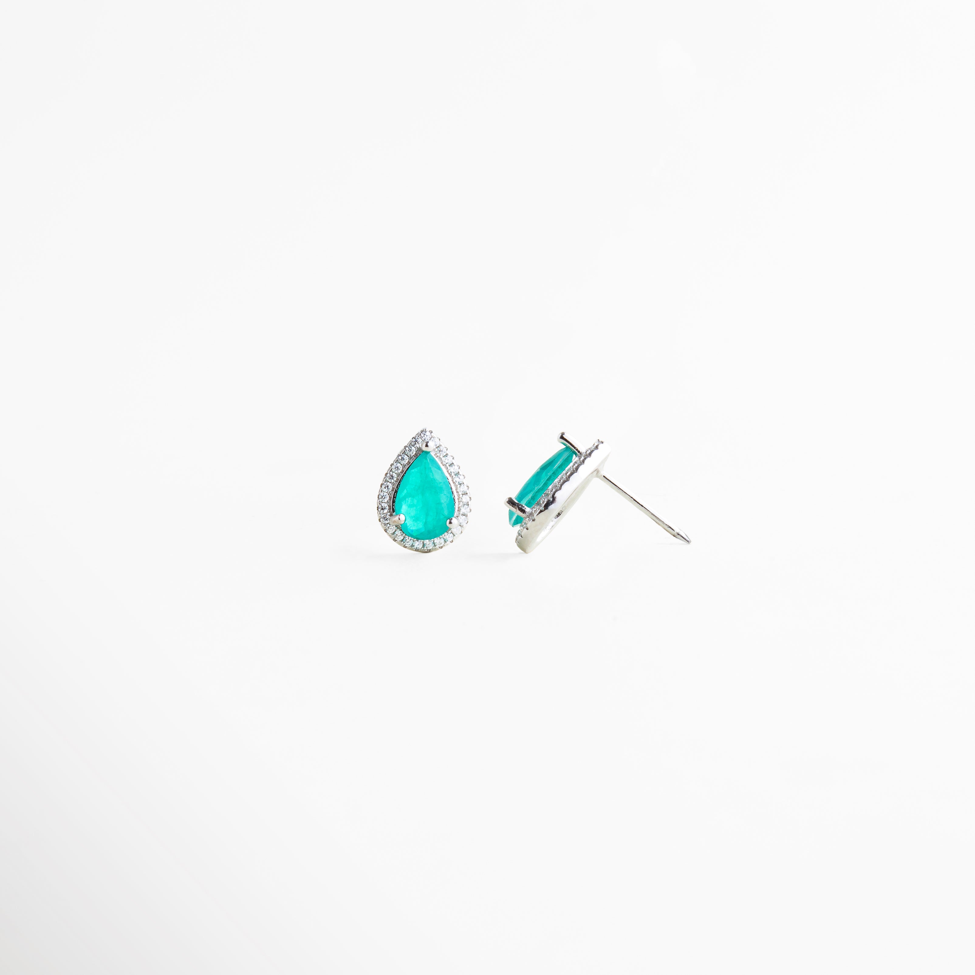 Aretes de plata ley 925 con broche tipo poste y piedra turquesa brillante, Vista inclinada de pendientes tipo gota con incrustaciones brillantes y acabado elegante, Detalle de aretes pequeños en plata con diseño sofisticado y cristales sintéticos, Pendientes de lágrima color turquesa con estructura fina y acabado brillante, Aretes minimalistas de plata con piedra azul turquesa y cierre clásico de poste.