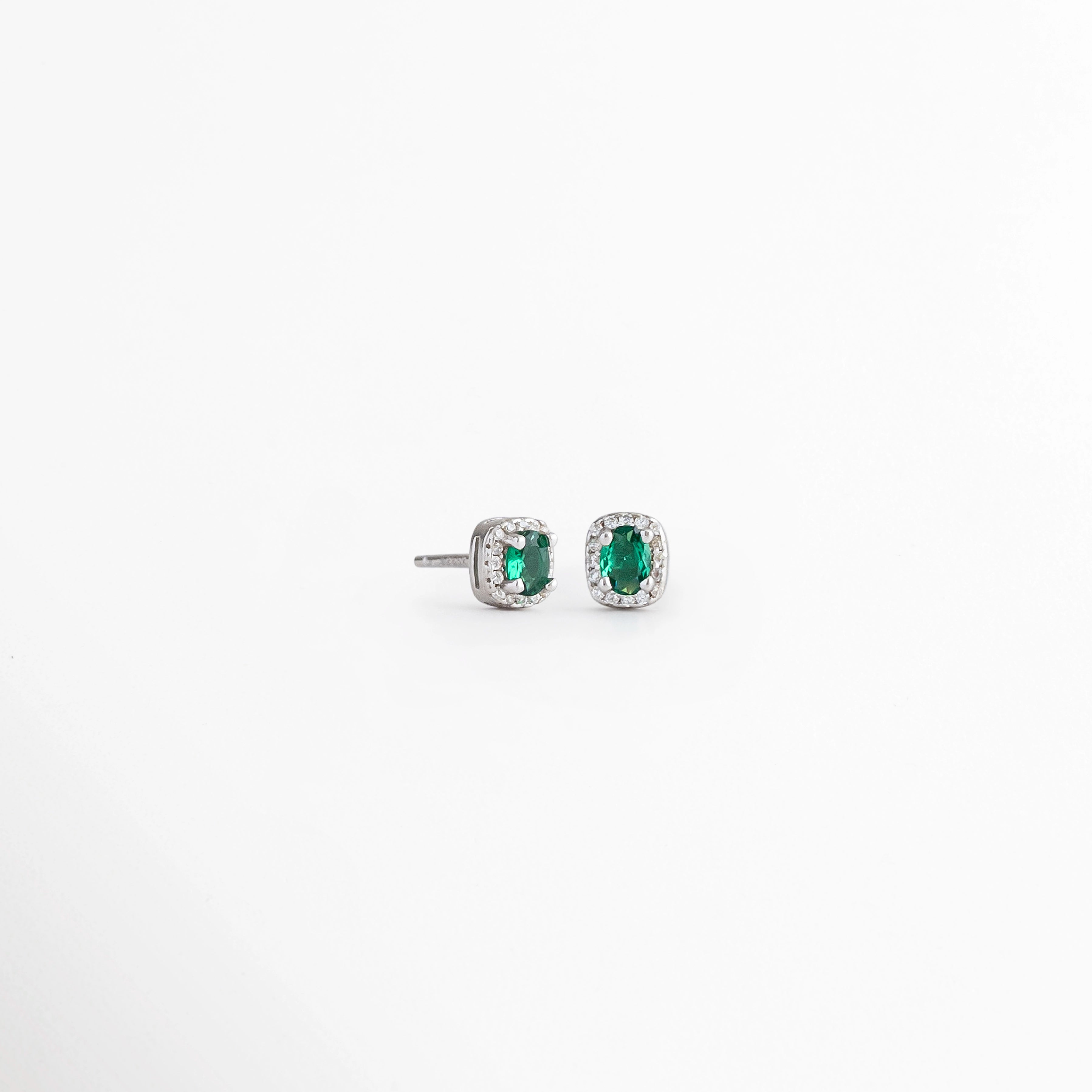 Vista en ángulo de los Aretes Alana Studs con esmeralda sintética y zirconias sobre Plata Ley 925, Perspectiva de los Aretes Alana Studs que resalta el brillo de la esmeralda sintética verde, Aretes Alana Studs fotografiados en ángulo mostrando la montura de Plata Esterlina, Vista diagonal de los Aretes Alana Studs con piedra verde ovalada y zirconias, Aretes de Plata Ley 925 Alana Studs con esmeralda sintética en vista de perspectiva.