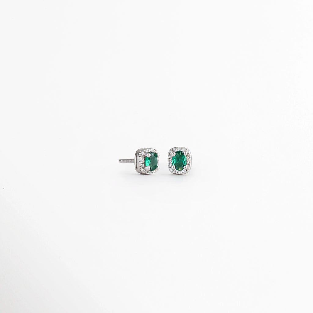 Vista en ángulo de los Aretes Alana Studs con esmeralda sintética y zirconias sobre Plata Ley 925, Perspectiva de los Aretes Alana Studs que resalta el brillo de la esmeralda sintética verde, Aretes Alana Studs fotografiados en ángulo mostrando la montura de Plata Esterlina, Vista diagonal de los Aretes Alana Studs con piedra verde ovalada y zirconias, Aretes de Plata Ley 925 Alana Studs con esmeralda sintética en vista de perspectiva.