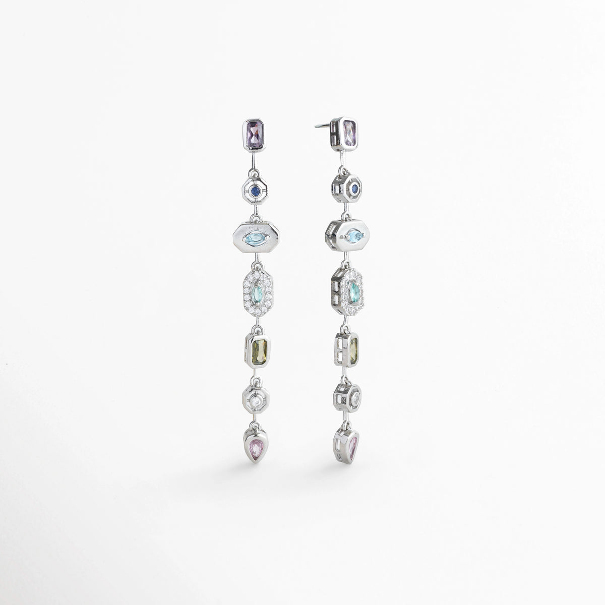 Vista en tres cuartos de los Aretes Silver Roux mostrando la fluidez y textura de la tira articulada con pedrería fina, Acercamiento en ángulo a la secuencia de gemas de colores y biseles decorativos en oro blanco 18K, Toma en perspectiva que destaca el reflejo de la luz en las gemas sintéticas multicolores de corte brillante, Muestra de la alineación estilizada y la caída fluida de 6.5 cm de los aretes colgantes sobre fondo claro.