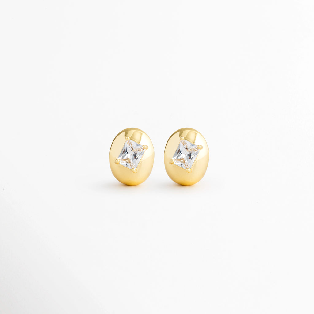 Aretes Piaf Hoops de cobre con recubrimiento en Oro 18K y zirconia central sobre fondo blanco, Vista frontal de los Aretes Piaf Hoops con diseño ovalado y zirconia brillante en acabado Oro 18K, Aretes Piaf Hoops con diseño elegante de aro ovalado y zirconia central, Par de Aretes Piaf Hoops con acabado en Oro 18K y piedra de zirconia, Aretes dorados Piaf Hoops con diseño minimalista y zirconia brillante.