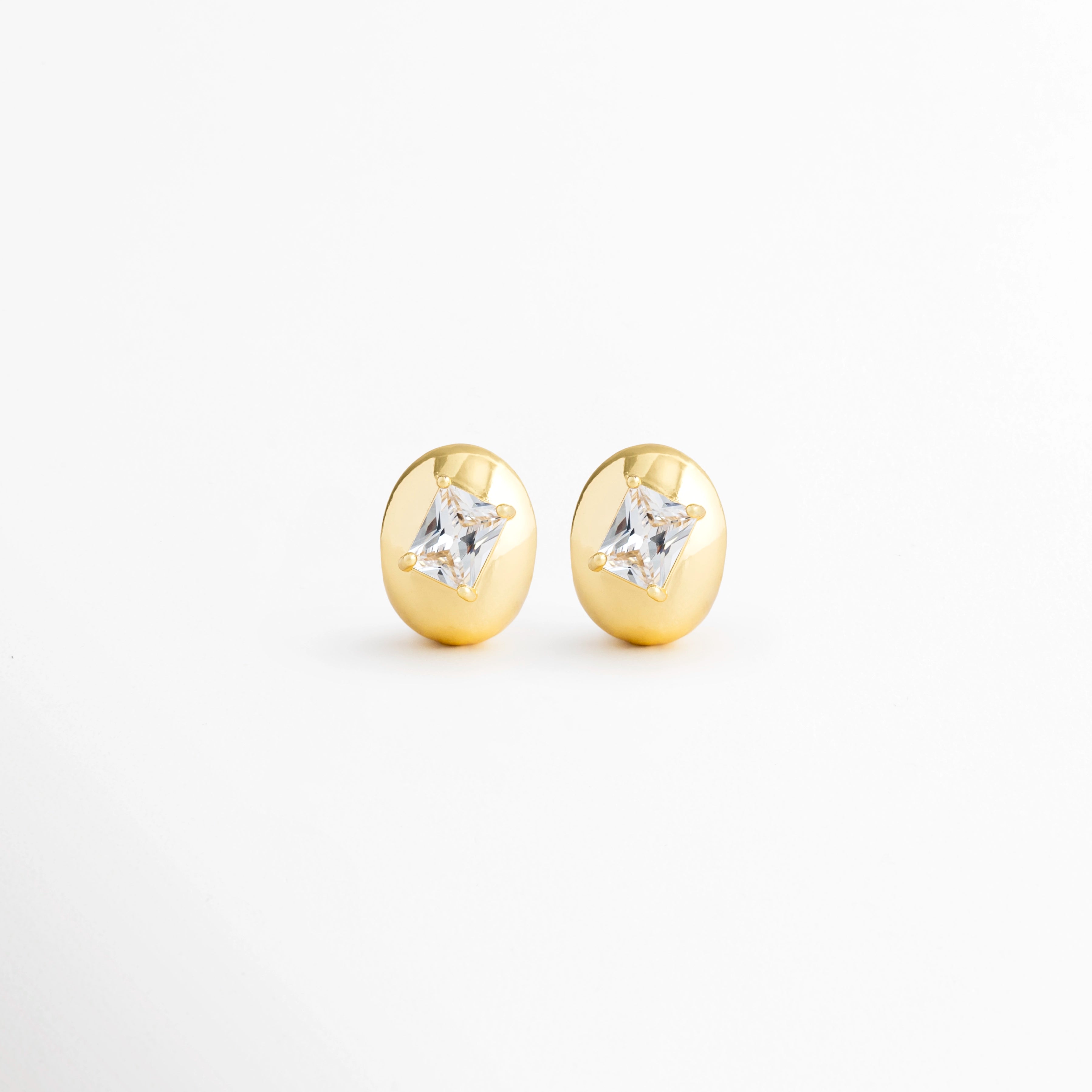 Aretes Piaf Hoops de cobre con recubrimiento en Oro 18K y zirconia central sobre fondo blanco, Vista frontal de los Aretes Piaf Hoops con diseño ovalado y zirconia brillante en acabado Oro 18K, Aretes Piaf Hoops con diseño elegante de aro ovalado y zirconia central, Par de Aretes Piaf Hoops con acabado en Oro 18K y piedra de zirconia, Aretes dorados Piaf Hoops con diseño minimalista y zirconia brillante.