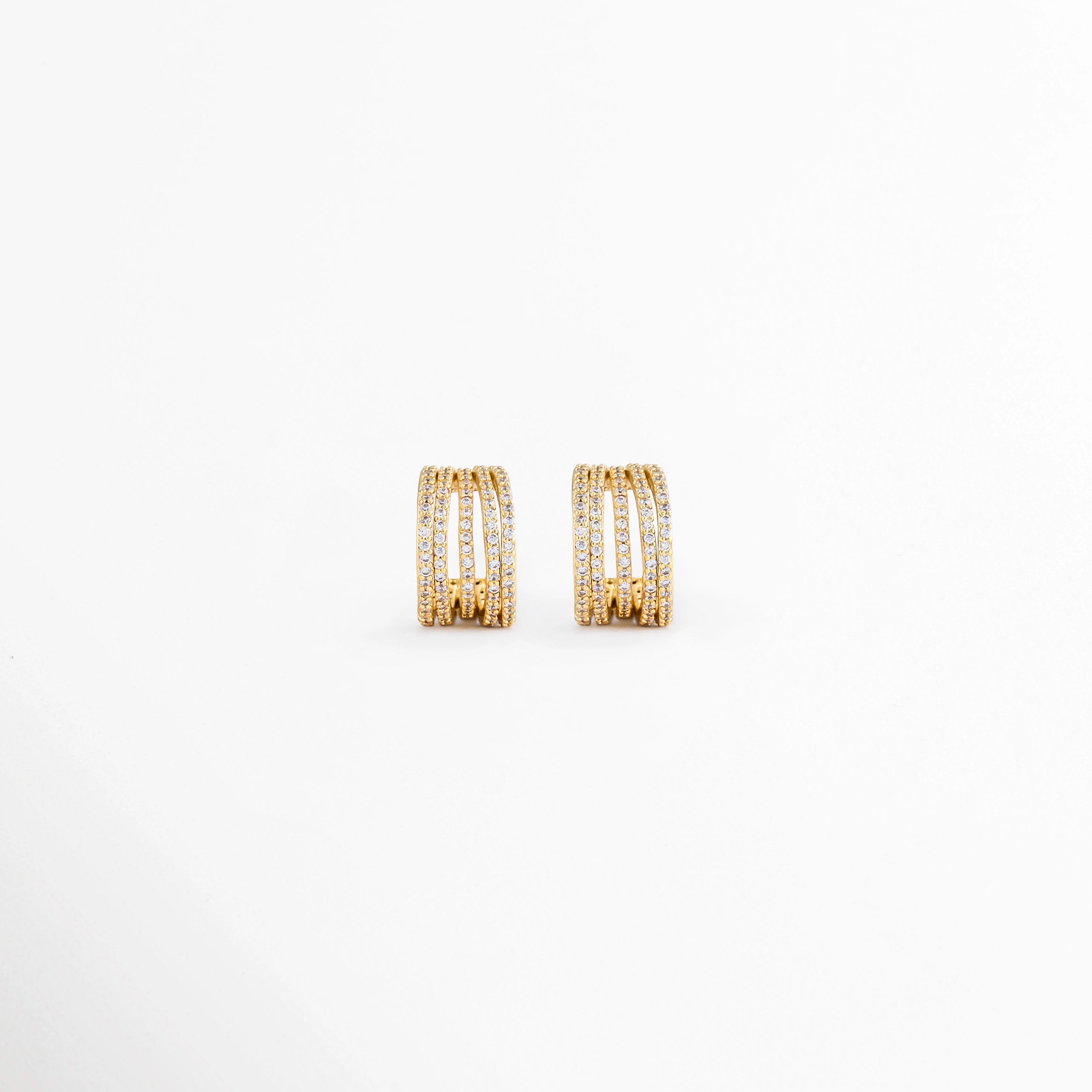 Aretes Jovovich Golden Hoops de cobre con recubrimiento en Oro y diseño tipo huggie con textura sobre fondo blanco, Vista frontal de los Aretes Jovovich Golden Hoops con acabado dorado brillante y diseño minimalista, Aretes Jovovich Golden Hoops con diseño de aro pequeño y textura elegante en acabado dorado, Par de Aretes Jovovich Golden Hoops elaborados en cobre con recubrimiento en Oro, Aretes dorados Jovovich Golden Hoops con diseño moderno tipo huggie y acabado brillante.