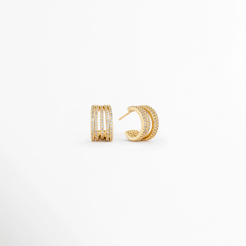 Vista en ángulo de los Aretes Jovovich Golden Hoops mostrando el perfil y el sistema de cierre, Perspectiva de los Aretes Jovovich Golden Hoops con acabado dorado y diseño tipo huggie, Aretes Jovovich Golden Hoops fotografiados de perfil resaltando su textura y brillo, Vista diagonal de los Aretes Jovovich Golden Hoops elaborados en cobre con recubrimiento en Oro, Aretes Jovovich Golden Hoops en perspectiva mostrando su diseño elegante y minimalista.