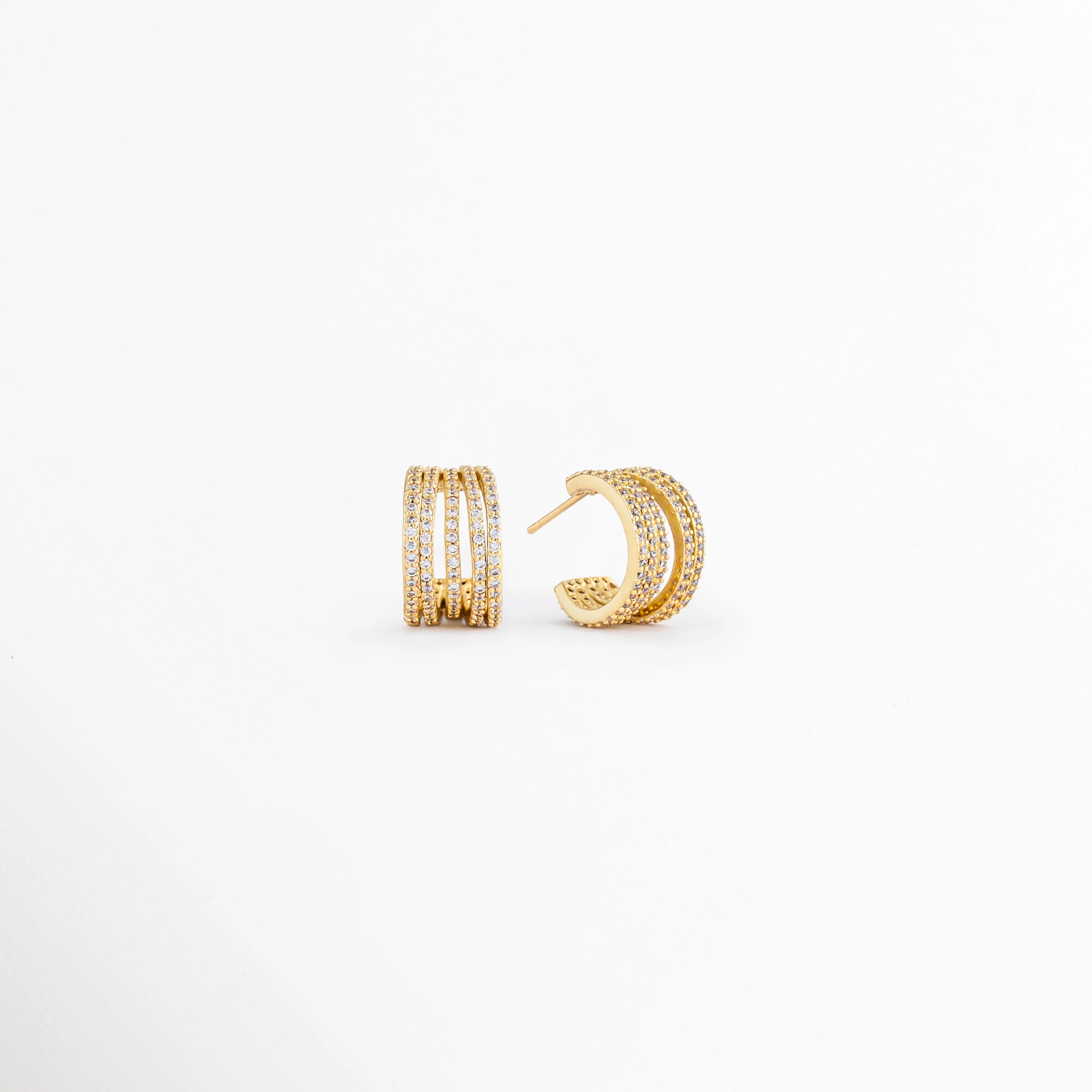 Vista en ángulo de los Aretes Jovovich Golden Hoops mostrando el perfil y el sistema de cierre, Perspectiva de los Aretes Jovovich Golden Hoops con acabado dorado y diseño tipo huggie, Aretes Jovovich Golden Hoops fotografiados de perfil resaltando su textura y brillo, Vista diagonal de los Aretes Jovovich Golden Hoops elaborados en cobre con recubrimiento en Oro, Aretes Jovovich Golden Hoops en perspectiva mostrando su diseño elegante y minimalista.