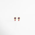 Aretes Winona Studs con zirconia violeta y zirconia fucsia en acabado dorado de 18K, Aretes pequeños dorados con zirconias en tonos violeta y fucsia, diseño delicado y femenino, Aretes tipo stud enchapados en oro 18K con zirconias de colores vibrantes, Aretes elegantes con zirconia violeta superior y zirconia fucsia inferior en diseño refinado, Aretes de latón con recubrimiento dorado y zirconias brillantes en tonos rosa y violeta.