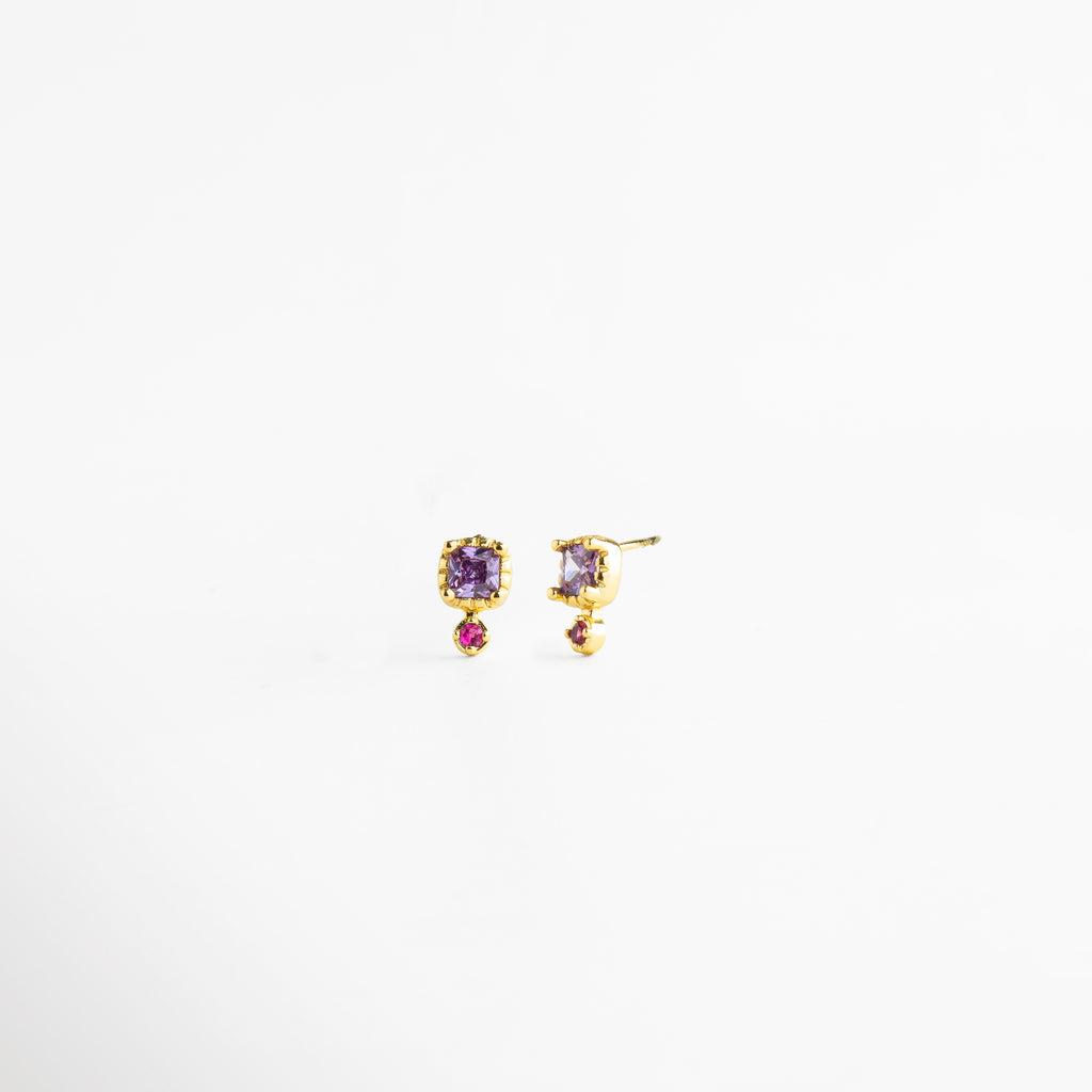 Vista lateral de aretes Winona Studs con zirconias en tonos violeta y fucsia, Aretes pequeños dorados con piedras zirconia coloridas vistos desde un ángulo lateral, Perfil de aretes tipo stud con acabado oro 18K y zirconias brillantes, Vista inclinada de aretes delicados con doble zirconia en tonos vibrantes, Aretes de latón con zirconias violetas y fucsias en vista lateral elegante.