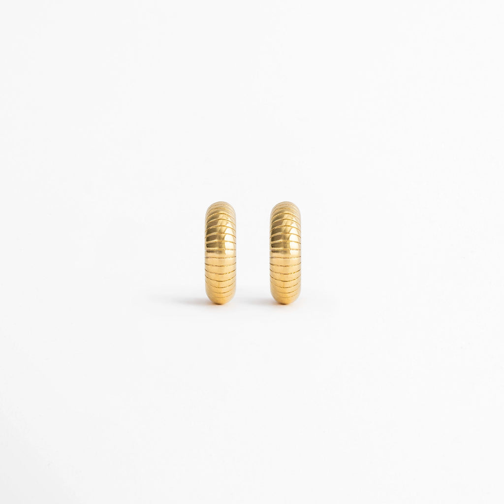 Aretes Golden Shell Hoops de acero inoxidable con recubrimiento en Oro 18K y diseño acanalado sobre fondo blanco, Vista frontal de los Aretes Golden Shell Hoops con acabado en Oro 18K y textura de inspiración concha,Aretes Golden Shell Hoops con diseño tipo huggie y acabado dorado brillante, Par de Aretes Golden Shell Hoops elaborados en acero inoxidable con textura acanalada, Aretes dorados Golden Shell Hoops con diseño clásico y acabado en Oro 18K.