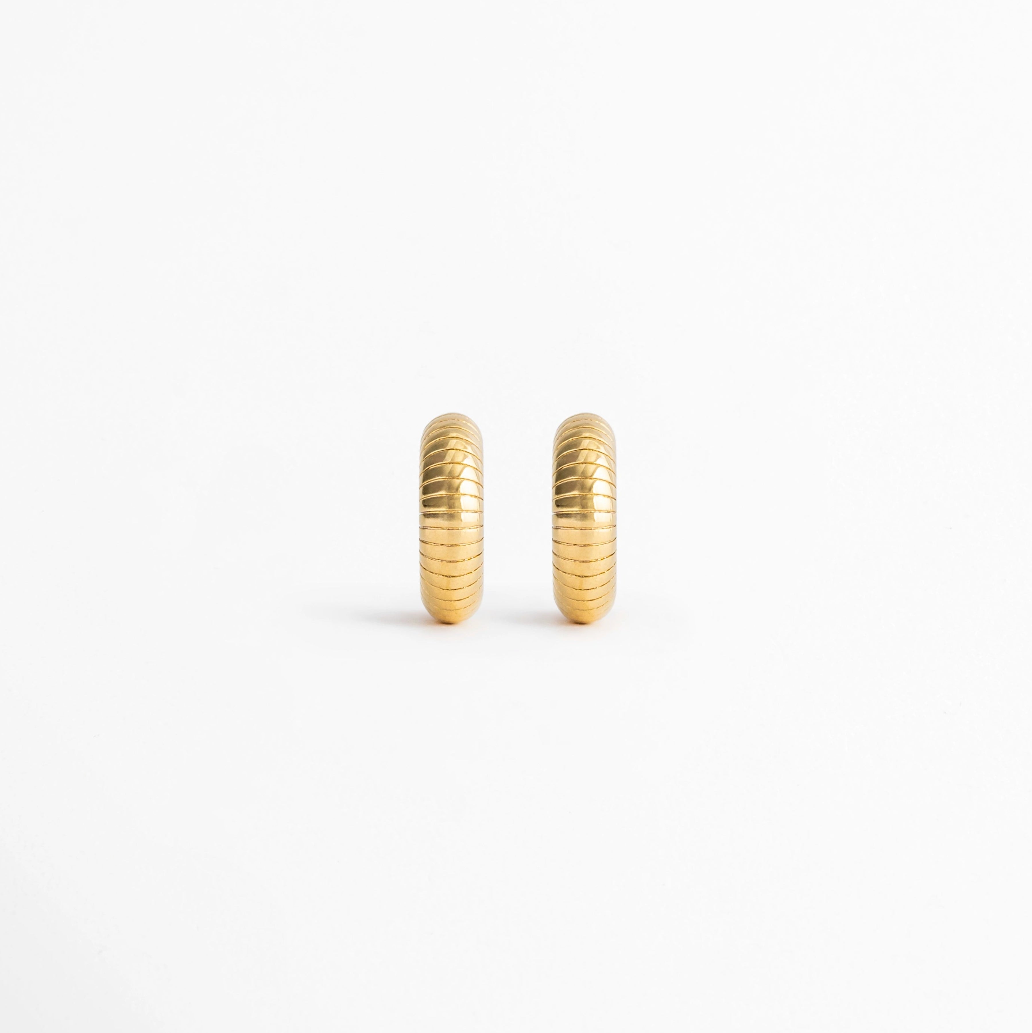Aretes Golden Shell Hoops de acero inoxidable con recubrimiento en Oro 18K y diseño acanalado sobre fondo blanco, Vista frontal de los Aretes Golden Shell Hoops con acabado en Oro 18K y textura de inspiración concha,Aretes Golden Shell Hoops con diseño tipo huggie y acabado dorado brillante, Par de Aretes Golden Shell Hoops elaborados en acero inoxidable con textura acanalada, Aretes dorados Golden Shell Hoops con diseño clásico y acabado en Oro 18K.