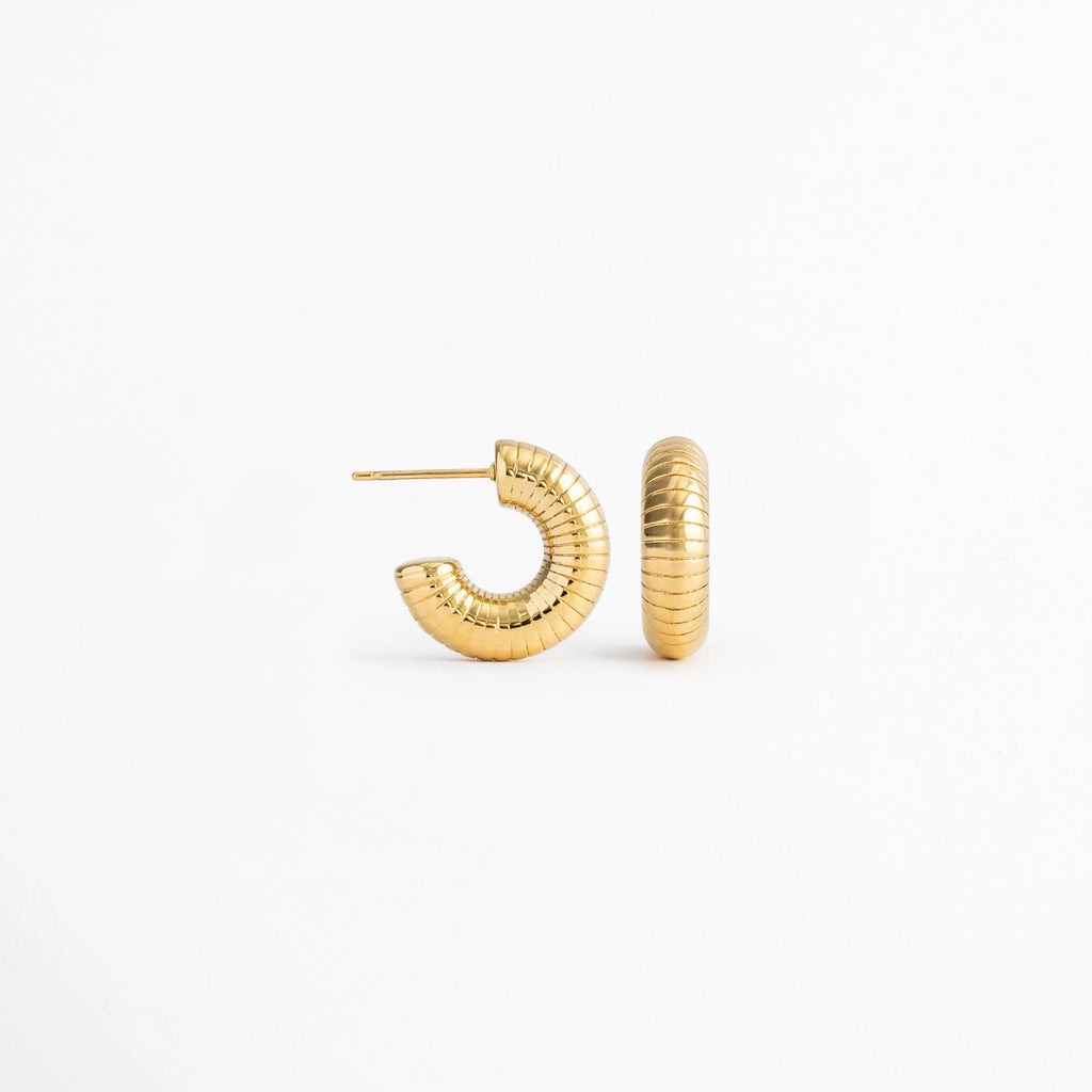 Vista lateral de los Aretes Golden Shell Hoops mostrando el cierre tipo bisagra y el perfil del aro, Perfil de los Aretes Golden Shell Hoops con acabado en Oro 18K y diseño acanalado, Aretes Golden Shell Hoops en vista lateral destacando el sistema de cierre y la textura del aro, Detalle lateral de los Aretes Golden Shell Hoops elaborados en acero inoxidable con acabado dorado, Vista de costado de los Aretes Golden Shell Hoops con diseño tipo huggie y acabado brillante.