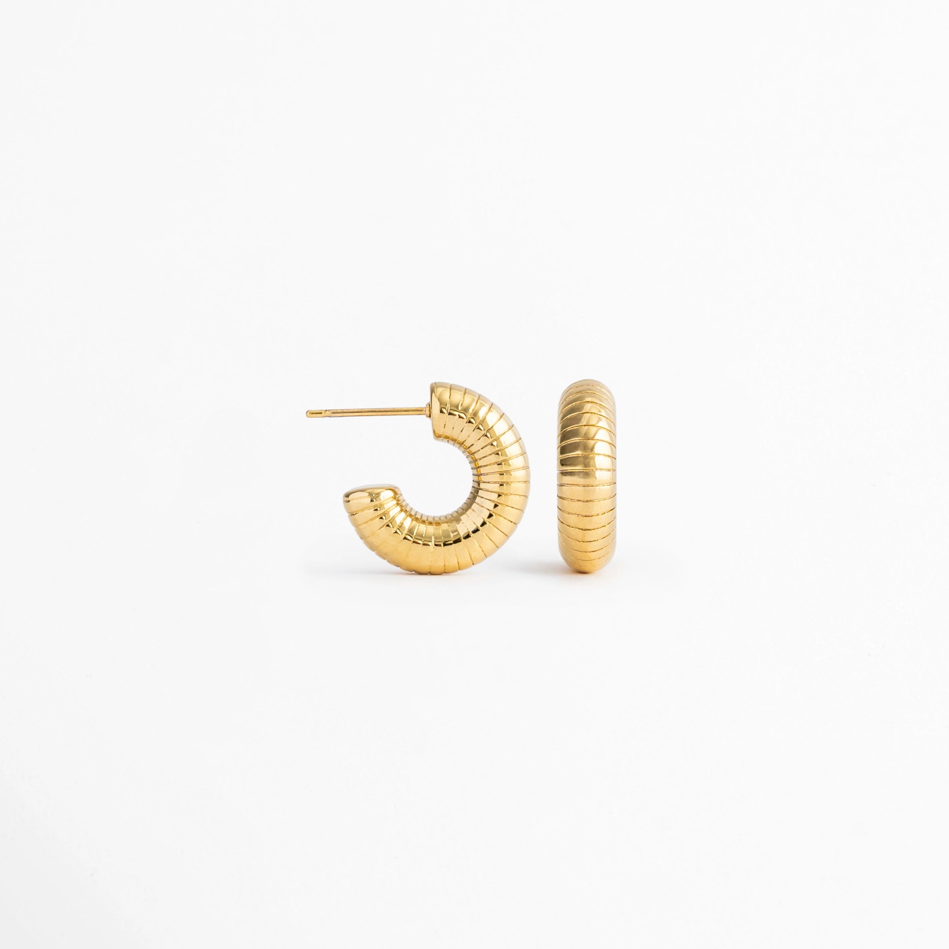 Vista lateral de los Aretes Golden Shell Hoops mostrando el cierre tipo bisagra y el perfil del aro, Perfil de los Aretes Golden Shell Hoops con acabado en Oro 18K y diseño acanalado, Aretes Golden Shell Hoops en vista lateral destacando el sistema de cierre y la textura del aro, Detalle lateral de los Aretes Golden Shell Hoops elaborados en acero inoxidable con acabado dorado, Vista de costado de los Aretes Golden Shell Hoops con diseño tipo huggie y acabado brillante.