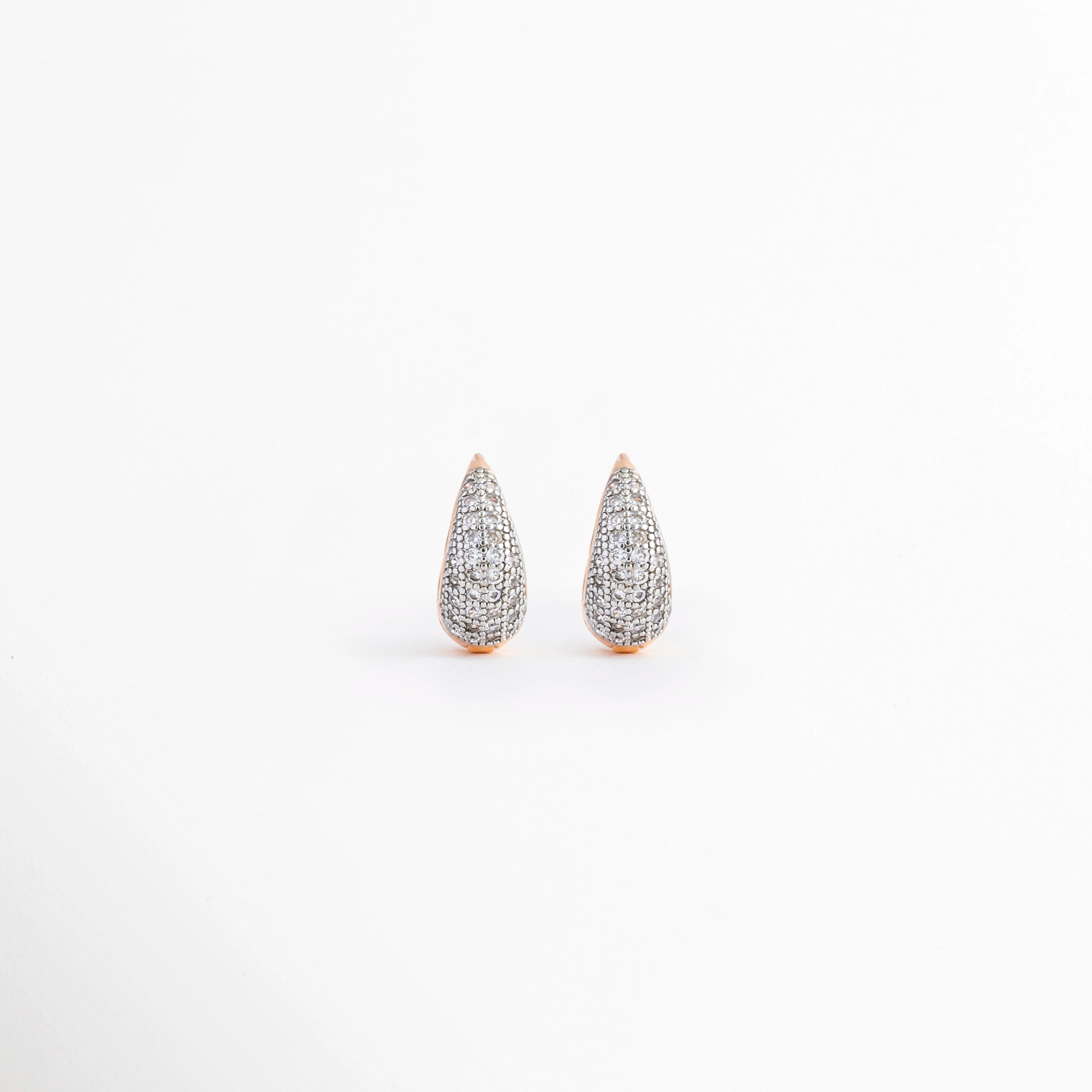 Aretes Zarya Golden Hoops de cobre con recubrimiento en Oro 18K e incrustaciones de zirconias sobre fondo blanco, Vista frontal de los Aretes Zarya Golden Hoops con diseño tipo huggie y zirconias brillantes, Aretes Zarya Golden Hoops con acabado en Oro 18K y detalle de zirconias incrustadas, Par de Aretes Zarya Golden Hoops con diseño elegante tipo aro y zirconias en acabado dorado, Aretes dorados Zarya Golden Hoops con zirconias y diseño clásico para mujer.
