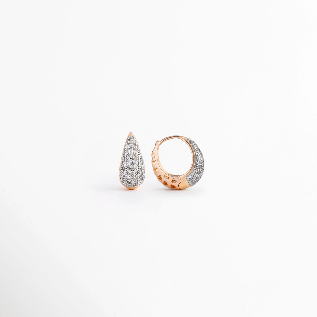 Vista en ángulo de los Aretes Zarya Golden Hoops mostrando el perfil y el brillo de las zirconias, Perspectiva de los Aretes Zarya Golden Hoops con acabado en Oro 18K y diseño tipo huggie, Aretes Zarya Golden Hoops fotografiados de perfil resaltando las zirconias incrustadas, Vista diagonal de los Aretes Zarya Golden Hoops elaborados en cobre con recubrimiento en Oro 18K, Aretes Zarya Golden Hoops en perspectiva mostrando su diseño elegante y acabado brillante.
