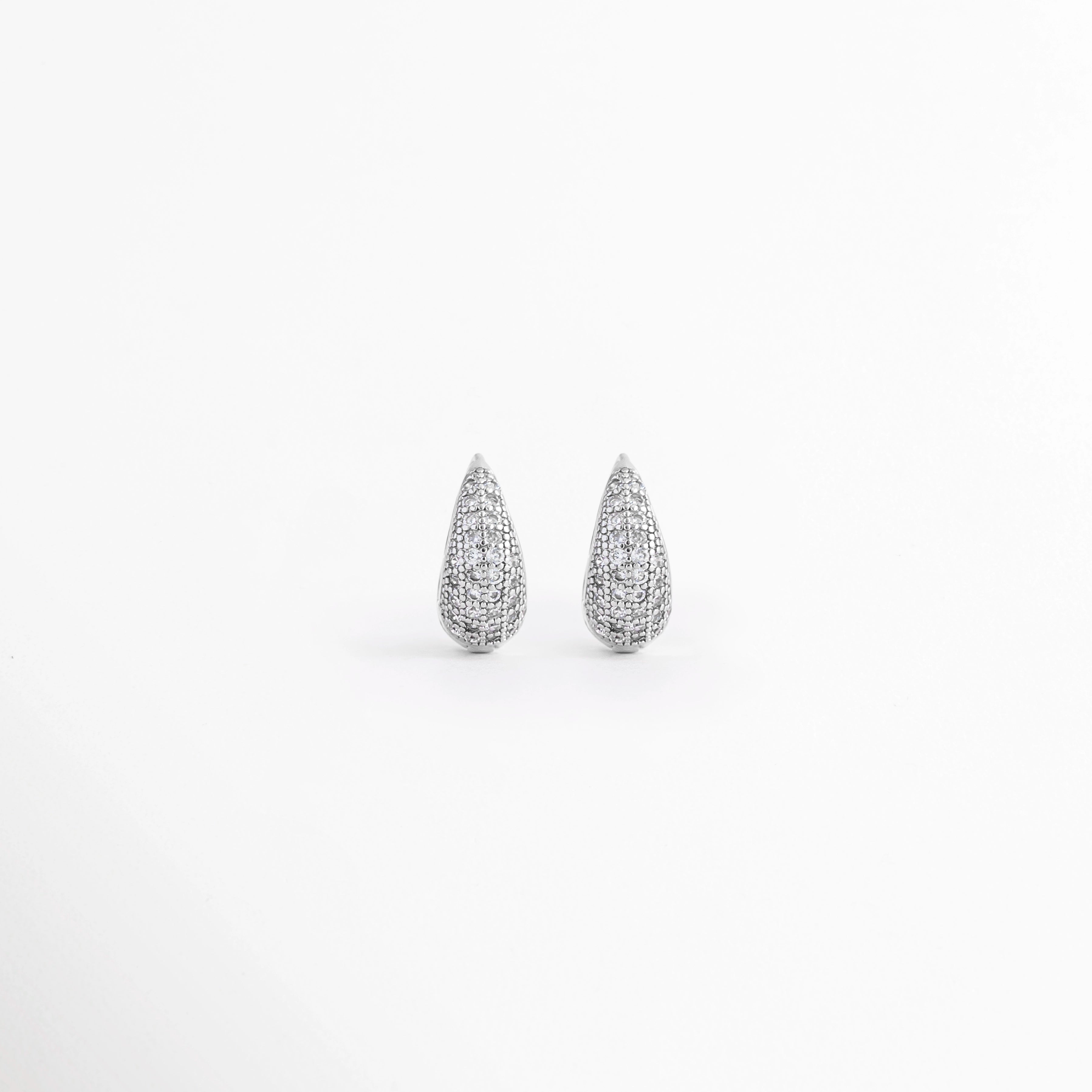 Aretes Zarya Silver Hoops de cobre con recubrimiento en Oro Blanco 18K e incrustaciones de zirconias sobre fondo blanco, Vista frontal de los Aretes Zarya Silver Hoops con diseño tipo huggie y zirconias brillantes, Aretes Zarya Silver Hoops con acabado en Oro Blanco 18K y detalle de zirconias en todo el frente, Par de Aretes Zarya Silver Hoops con diseño elegante tipo aro y zirconias incrustadas, Aretes plateados Zarya Silver Hoops con acabado brillante y diseño clásico con zirconias.