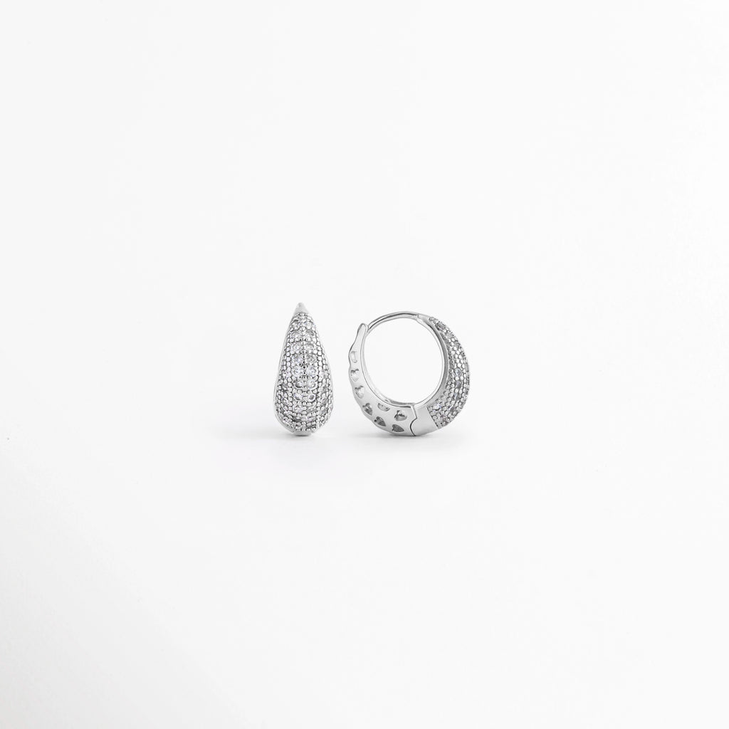 Vista en ángulo de los Aretes Zarya Silver Hoops mostrando el perfil y el brillo de las zirconias, Perspectiva de los Aretes Zarya Silver Hoops con acabado en Oro Blanco 18K y diseño tipo huggie, Aretes Zarya Silver Hoops fotografiados de perfil resaltando las zirconias incrustadas, Vista diagonal de los Aretes Zarya Silver Hoops elaborados en cobre con acabado plateado brillante, Aretes Zarya Silver Hoops en perspectiva mostrando su diseño elegante y minimalista.
