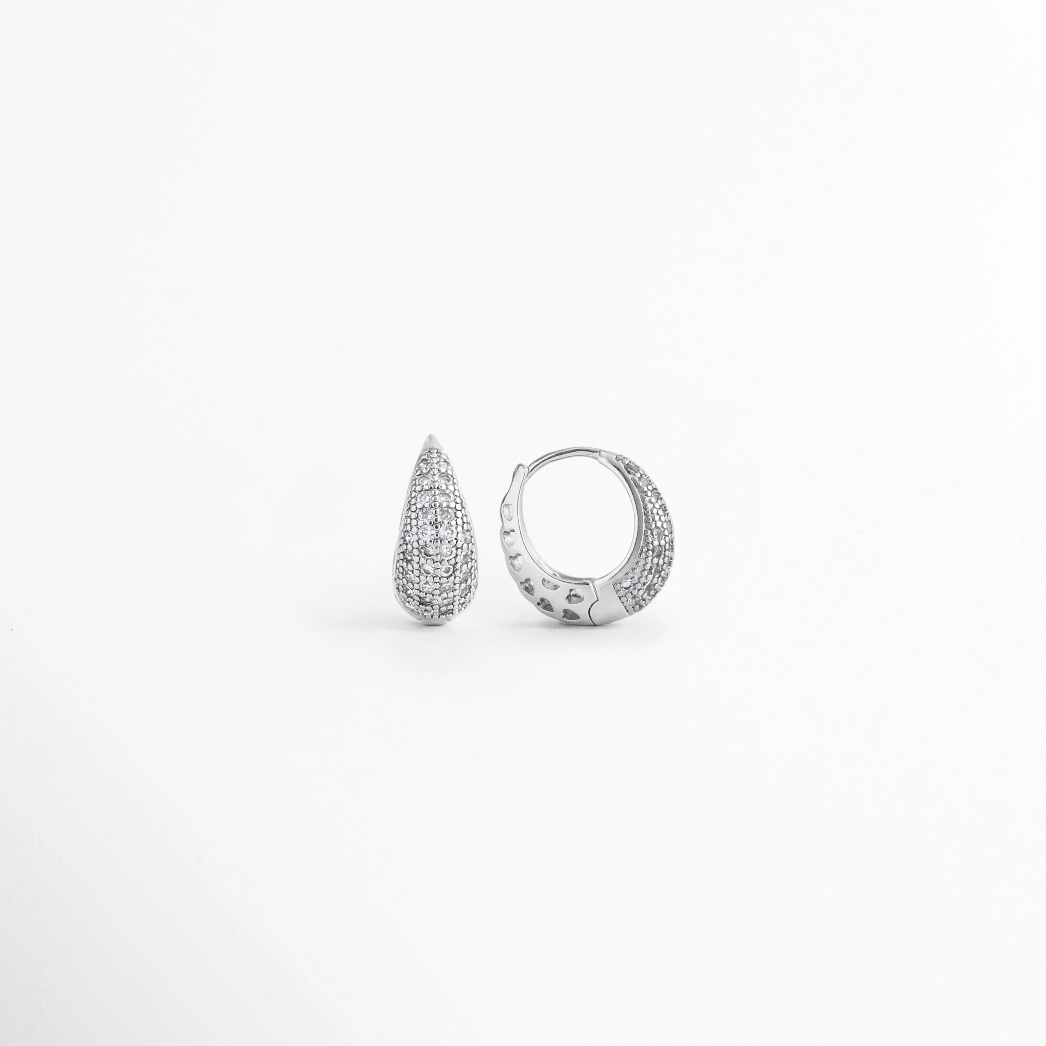 Vista en ángulo de los Aretes Zarya Silver Hoops mostrando el perfil y el brillo de las zirconias, Perspectiva de los Aretes Zarya Silver Hoops con acabado en Oro Blanco 18K y diseño tipo huggie, Aretes Zarya Silver Hoops fotografiados de perfil resaltando las zirconias incrustadas, Vista diagonal de los Aretes Zarya Silver Hoops elaborados en cobre con acabado plateado brillante, Aretes Zarya Silver Hoops en perspectiva mostrando su diseño elegante y minimalista.