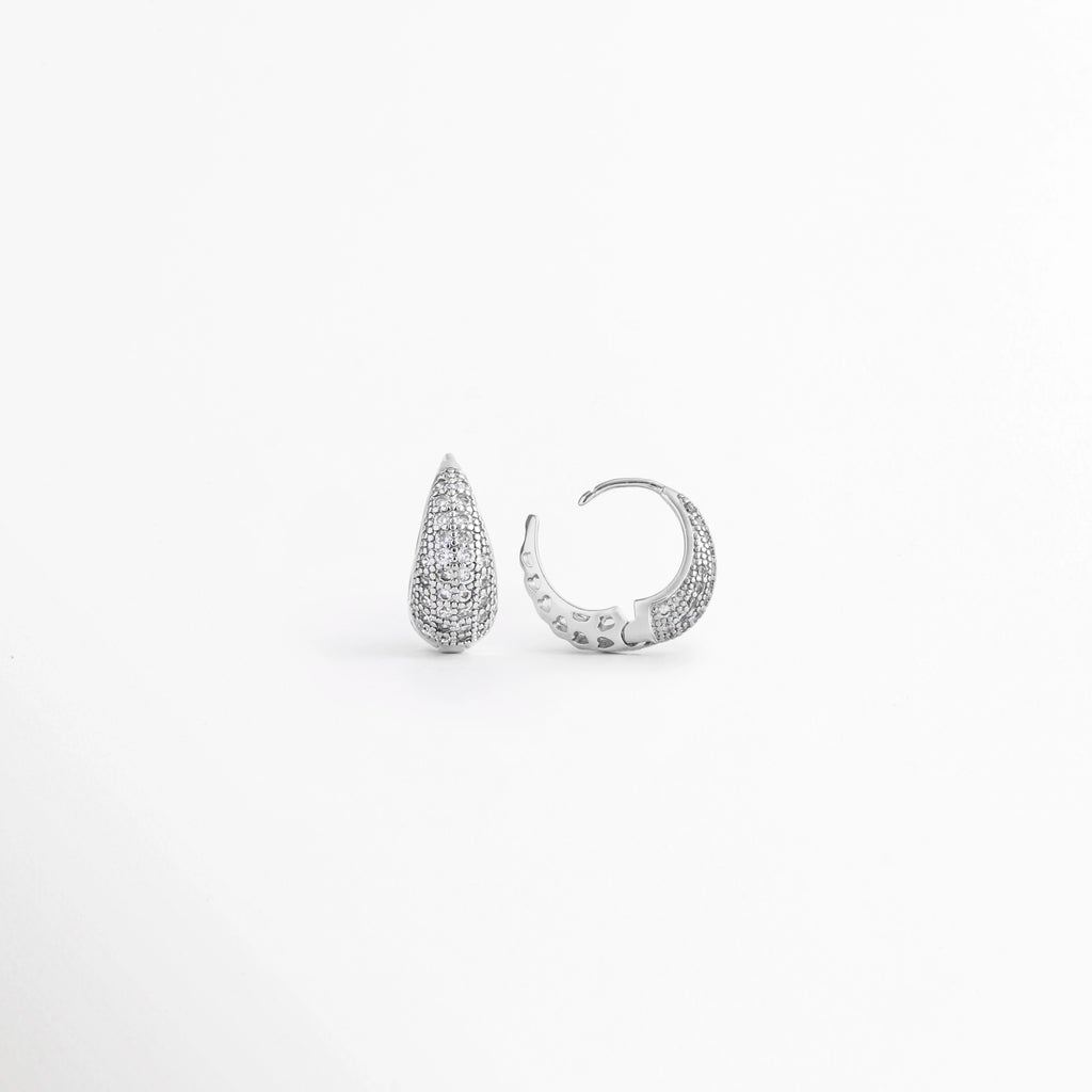 Vista lateral de los Aretes Zarya Silver Hoops mostrando el cierre tipo bisagra y el perfil del aro, Perfil de los Aretes Zarya Silver Hoops con acabado en Oro Blanco 18K y zirconias brillantes, Aretes Zarya Silver Hoops en vista lateral destacando el grosor del aro y el sistema de cierre, Detalle lateral de los Aretes Zarya Silver Hoops elaborados en cobre con incrustaciones de zirconias, Vista de costado de los Aretes Zarya Silver Hoops con diseño tipo huggie y acabado plateado.