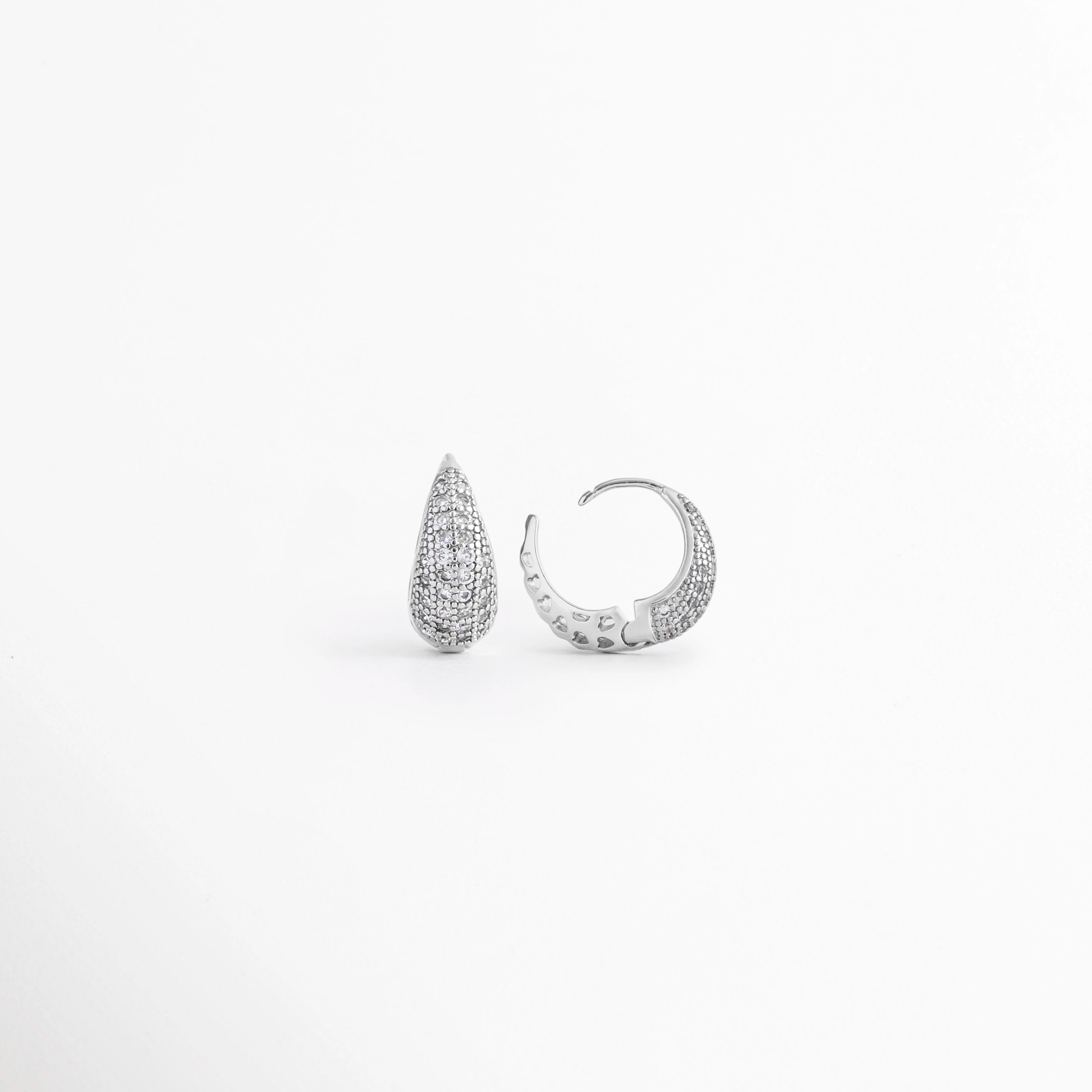 Vista lateral de los Aretes Zarya Silver Hoops mostrando el cierre tipo bisagra y el perfil del aro, Perfil de los Aretes Zarya Silver Hoops con acabado en Oro Blanco 18K y zirconias brillantes, Aretes Zarya Silver Hoops en vista lateral destacando el grosor del aro y el sistema de cierre, Detalle lateral de los Aretes Zarya Silver Hoops elaborados en cobre con incrustaciones de zirconias, Vista de costado de los Aretes Zarya Silver Hoops con diseño tipo huggie y acabado plateado.