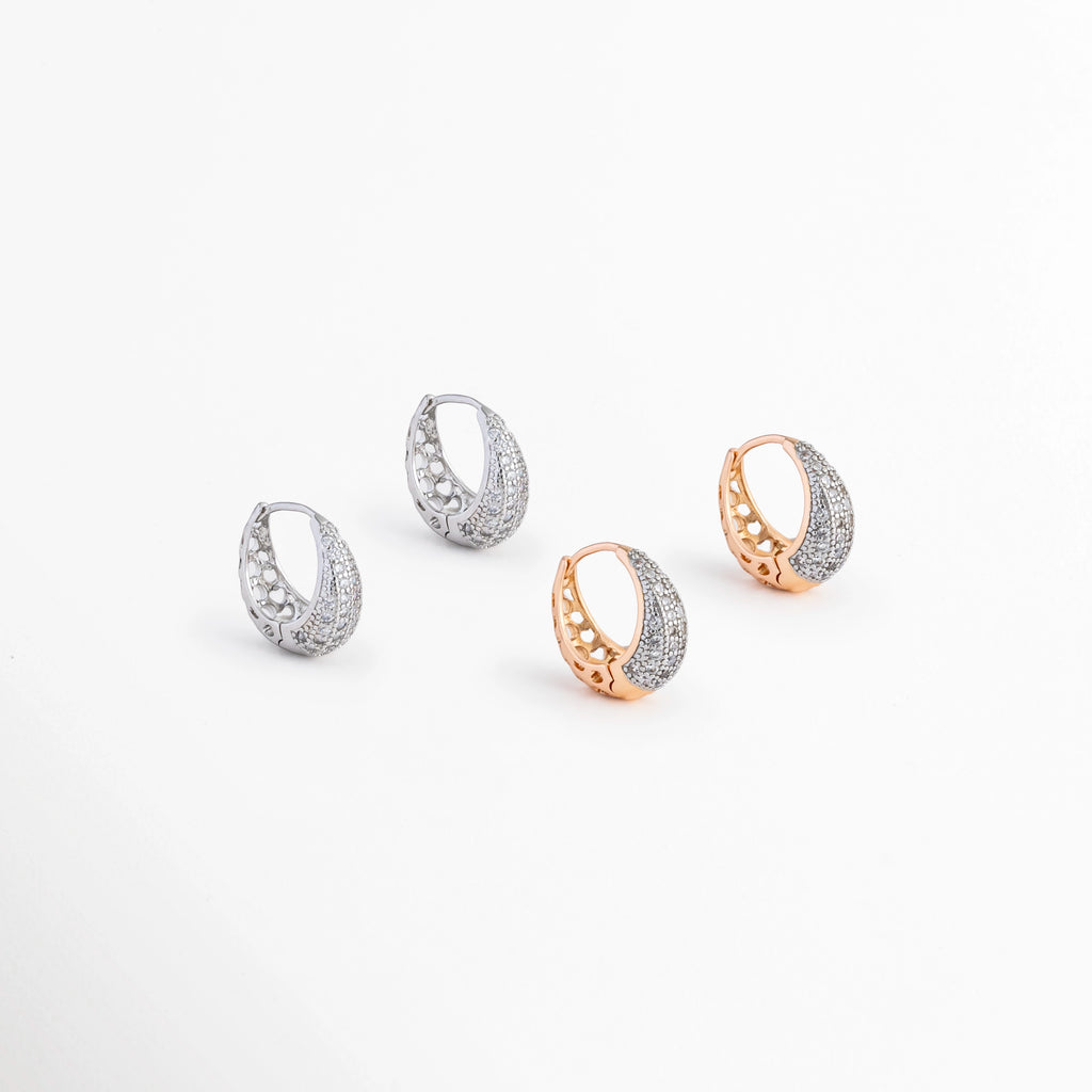 Aretes Zarya Hoops disponibles en acabados Oro Blanco 18K y Oro 18K con incrustaciones de zirconias, Comparativa de los Aretes Zarya Hoops en color plateado y dorado sobre fondo blanco, Variantes de color de los Aretes Zarya Hoops con zirconias y acabado brillante, Aretes Zarya Hoops mostrando las versiones plateada y dorada del mismo diseño tipo huggie, Vista comparativa de los Aretes Zarya Hoops disponibles en acabado plateado y dorado.