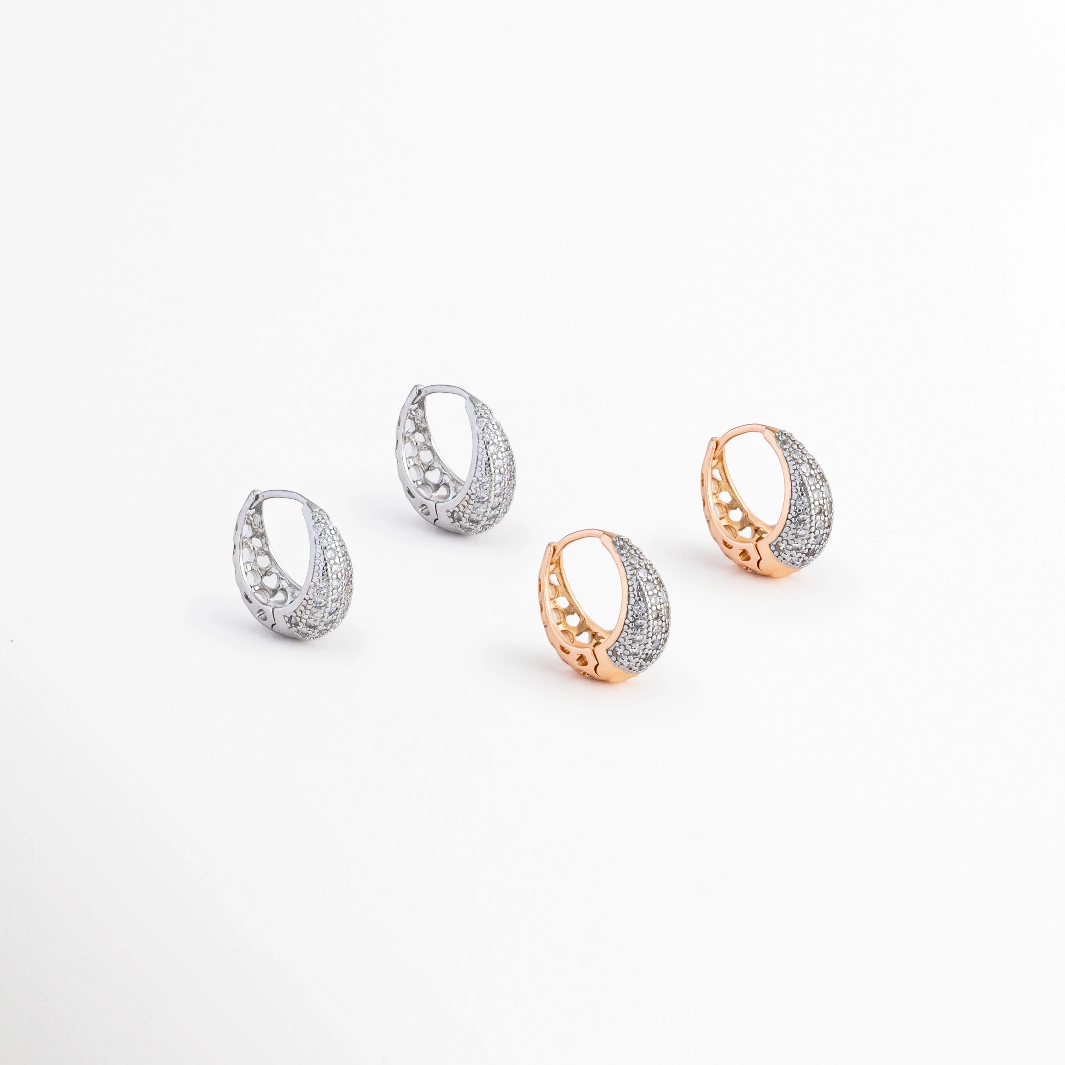 Aretes Zarya Hoops disponibles en acabados Oro Blanco 18K y Oro 18K con incrustaciones de zirconias, Comparativa de los Aretes Zarya Hoops en color plateado y dorado sobre fondo blanco, Variantes de color de los Aretes Zarya Hoops con zirconias y acabado brillante, Aretes Zarya Hoops mostrando las versiones plateada y dorada del mismo diseño tipo huggie, Vista comparativa de los Aretes Zarya Hoops disponibles en acabado plateado y dorado.
