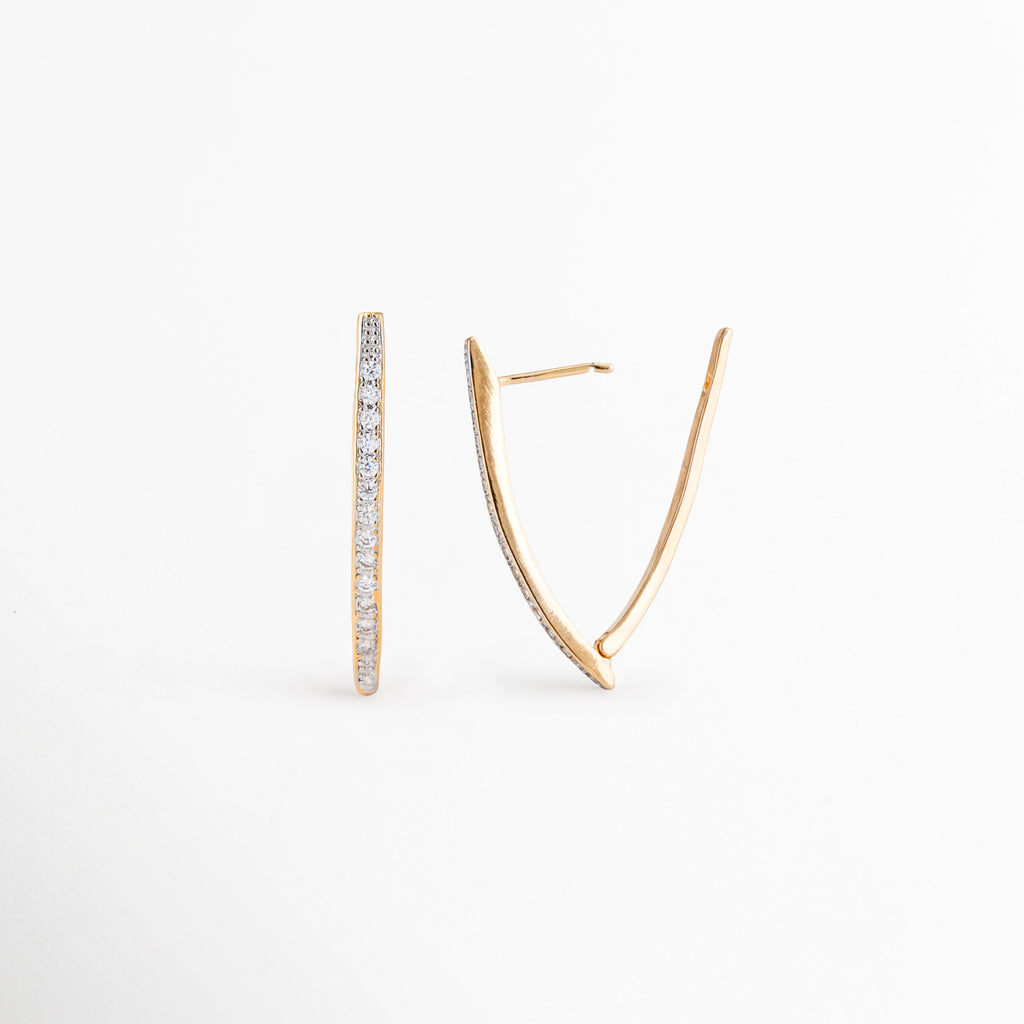 Aretes Regina desde ángulo lateral mostrando su diseño alargado, Detalle de aretes dorados con zirconias y acabado brillante, Vista angular de aretes modernos que enmarcan el rostro, Aretes largos con diseño geométrico y brillo elegante, Detalle de aretes statement dorados con zirconias.