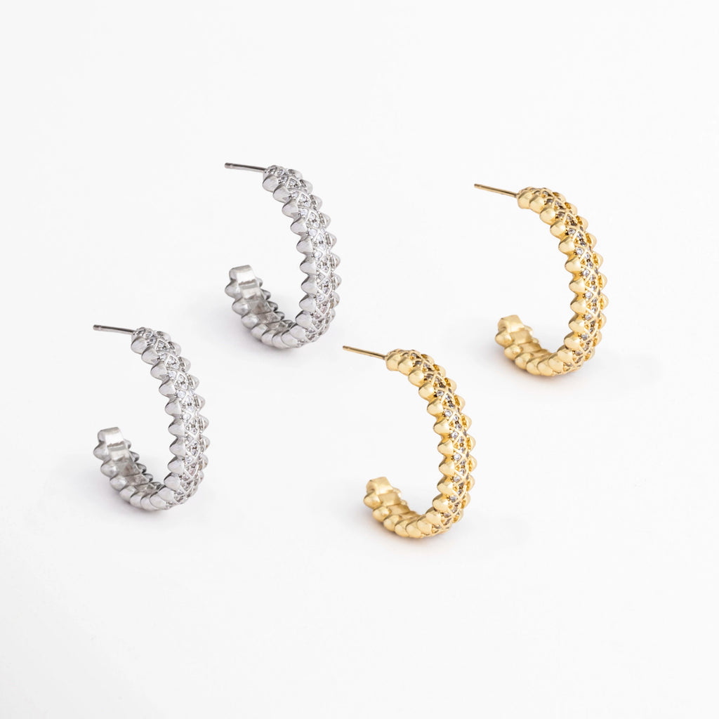 Aretes Azira disponibles en acabados Oro Blanco y Oro con incrustaciones de zirconias, Comparativa de los Aretes Azira en color plateado y dorado sobre fondo blanco, Variantes de color de los Aretes Azira con diseño lineal y zirconias, Aretes Azira mostrando las versiones plateada y dorada del mismo diseño contemporáneo, Vista comparativa de los Aretes Azira disponibles en acabado plateado y dorado.