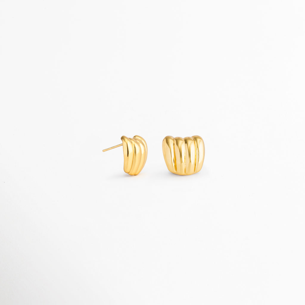 Perfil de los aretes Aurelia Studs con estructura curva y acabado dorado, Vista lateral de aretes minimalistas de acero inoxidable con baño de oro 18K, Detalle del diseño moderno de los Aurelia Studs en acabado dorado brillante, Aretes tipo poste dorados con forma orgánica y elegante, Vista de perfil de aretes pequeños dorados para uso diario.