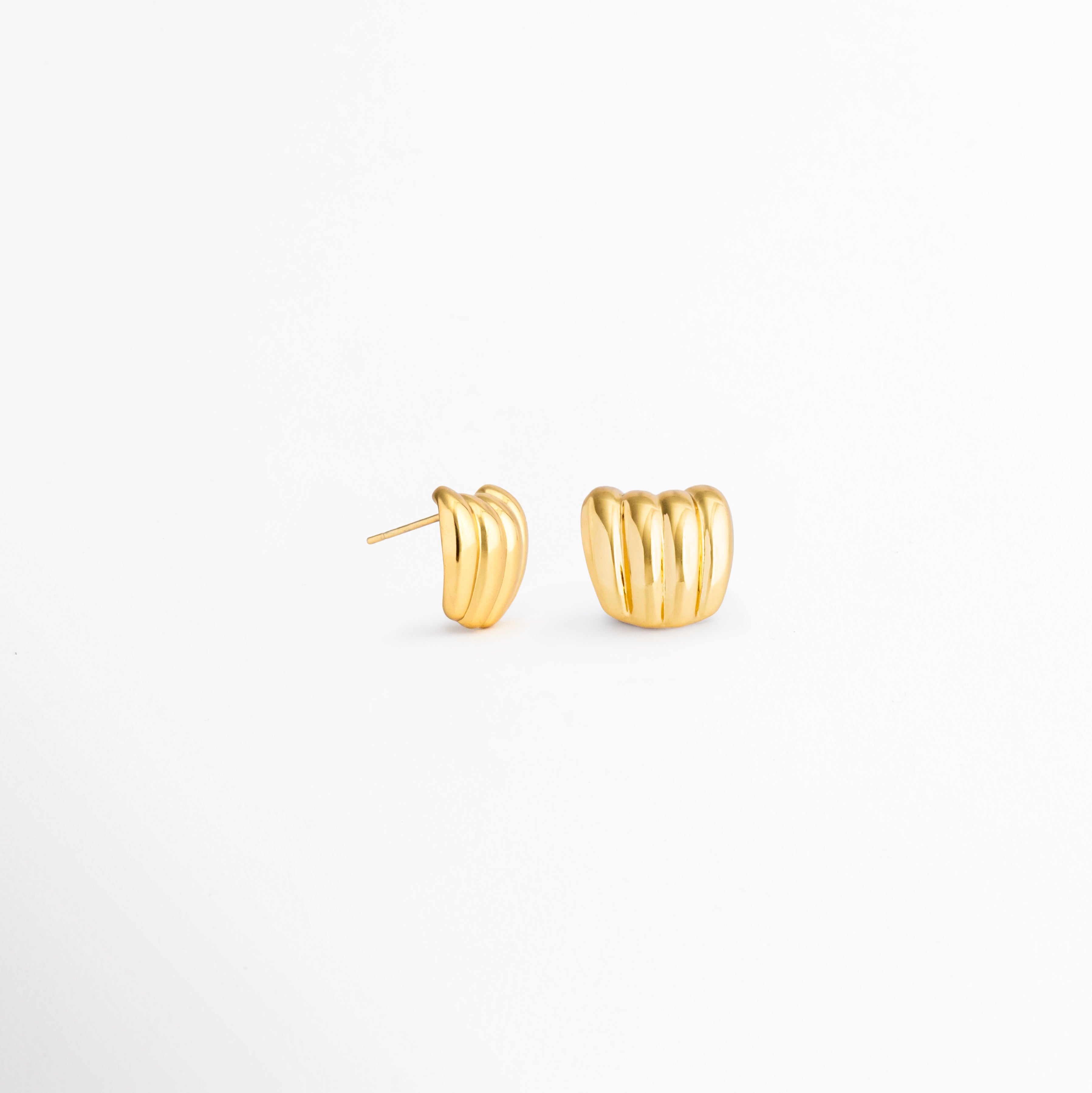 Perfil de los aretes Aurelia Studs con estructura curva y acabado dorado, Vista lateral de aretes minimalistas de acero inoxidable con baño de oro 18K, Detalle del diseño moderno de los Aurelia Studs en acabado dorado brillante, Aretes tipo poste dorados con forma orgánica y elegante, Vista de perfil de aretes pequeños dorados para uso diario.
