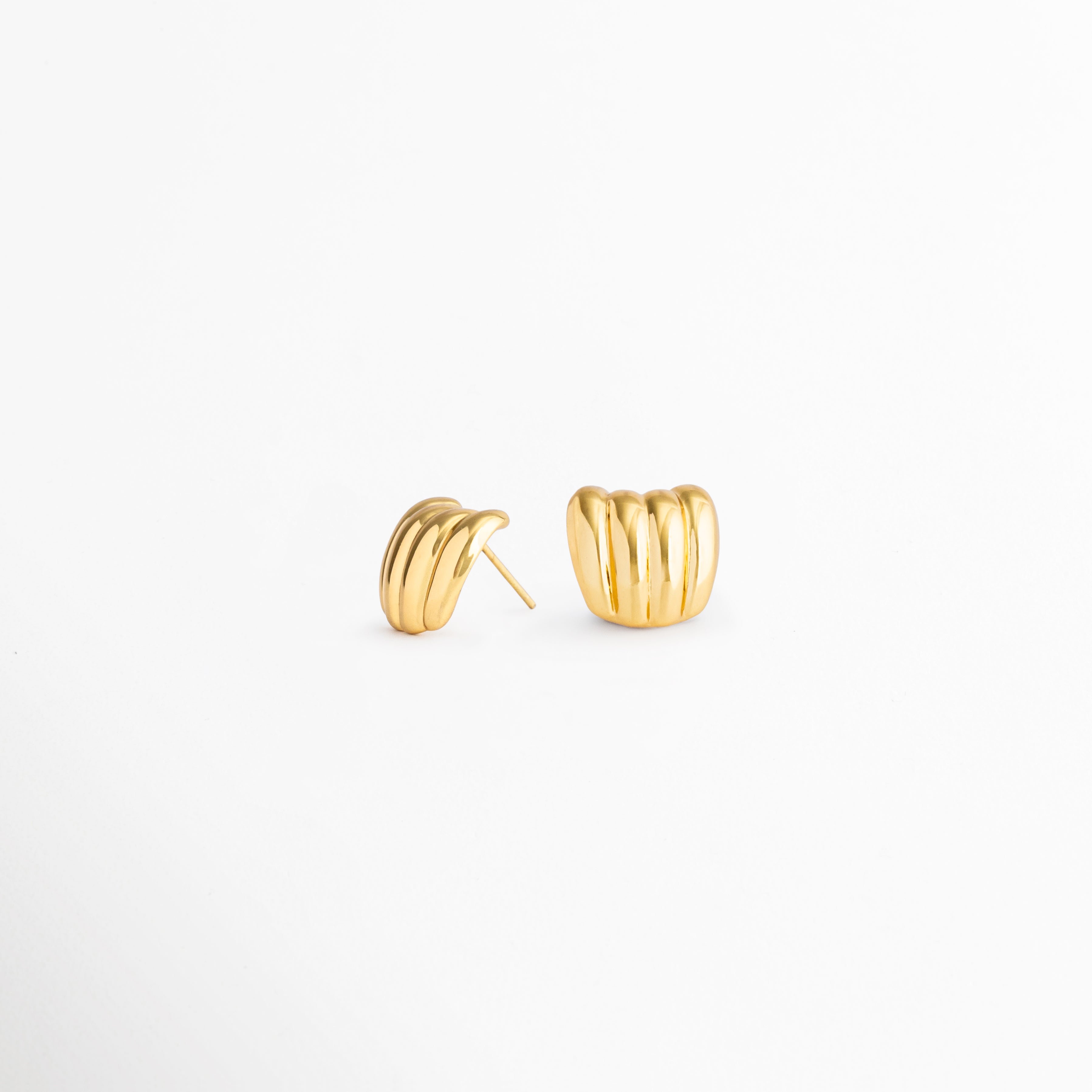 Detalle de los Aurelia Studs con acabado en oro 18K y diseño contemporáneo, Aretes dorados de acero inoxidable con textura acanalada y estilo minimalista, Vista cercana de aretes elegantes para mujer con líneas suaves y modernas, Aurelia Studs dorados, un diseño versátil para ocasiones casuales y especiales, Detalle de aretes pequeños con acabado brillante y forma curva sofisticada.
