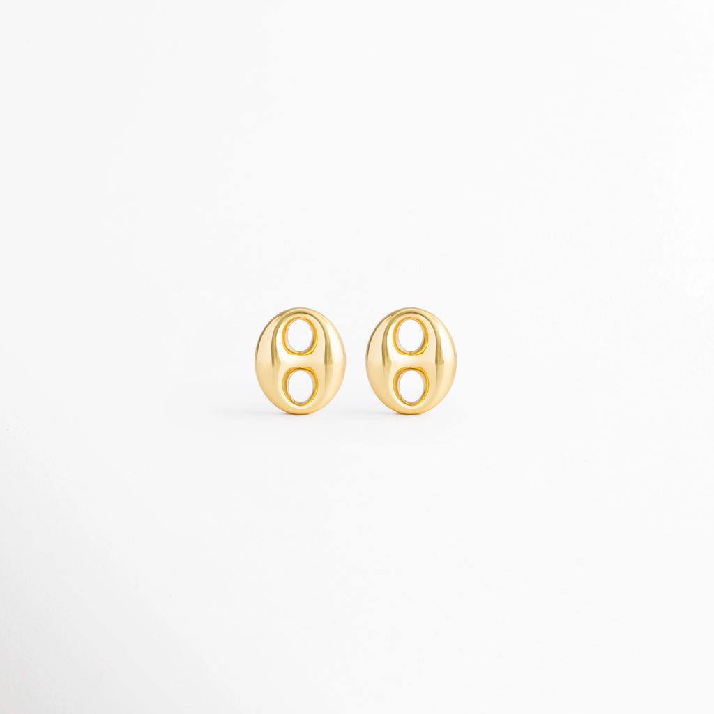 Aretes Sahra Golden Studs de acero inoxidable con recubrimiento en Oro 18K y diseño geométrico ovalado sobre fondo blanco, Vista frontal de los Aretes Sahra Golden Studs con acabado brillante en Oro 18K y estilo moderno, Aretes Sahra Golden Studs con diseño ovalado minimalista elaborados en acero inoxidable con acabado dorado, Par de Aretes Sahra Golden Studs con diseño contemporáneo y recubrimiento en Oro 18K, Aretes dorados Sahra Golden Studs de acero inoxidable con diseño geométrico elegante.