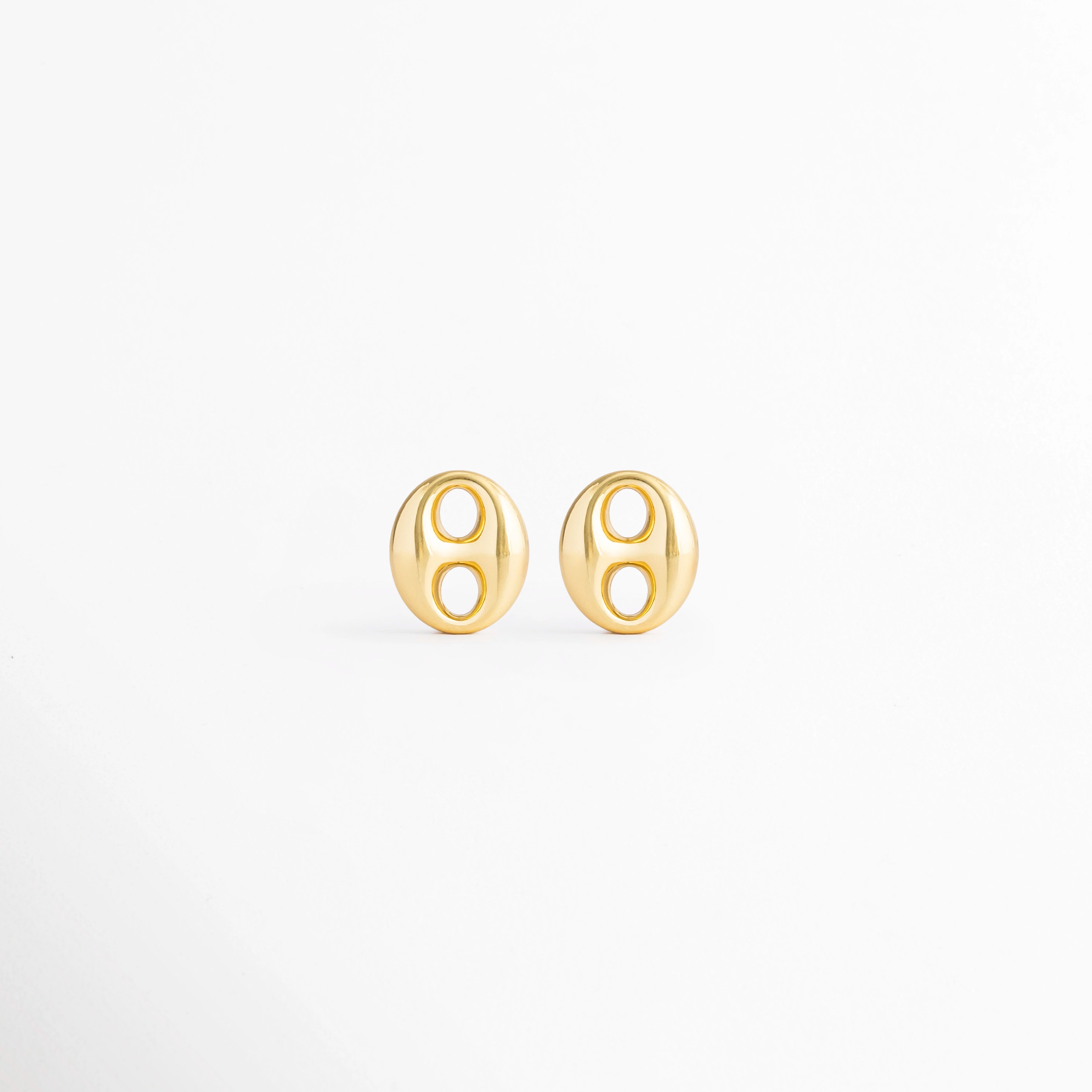 Aretes Sahra Golden Studs de acero inoxidable con recubrimiento en Oro 18K y diseño geométrico ovalado sobre fondo blanco, Vista frontal de los Aretes Sahra Golden Studs con acabado brillante en Oro 18K y estilo moderno, Aretes Sahra Golden Studs con diseño ovalado minimalista elaborados en acero inoxidable con acabado dorado, Par de Aretes Sahra Golden Studs con diseño contemporáneo y recubrimiento en Oro 18K, Aretes dorados Sahra Golden Studs de acero inoxidable con diseño geométrico elegante.