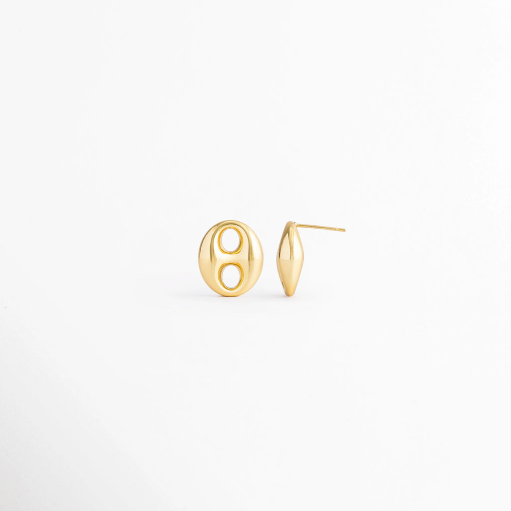 Vista en ángulo de los Aretes Sahra Golden Studs mostrando el perfil y el broche tipo poste, Perspectiva de los Aretes Sahra Golden Studs con acabado en Oro 18K y diseño geométrico ovalado, Aretes Sahra Golden Studs fotografiados de perfil resaltando el acabado dorado brillante, Vista diagonal de los Aretes Sahra Golden Studs elaborados en acero inoxidable con recubrimiento en Oro 18K, Aretes Sahra Golden Studs en perspectiva mostrando su estructura y diseño minimalista.