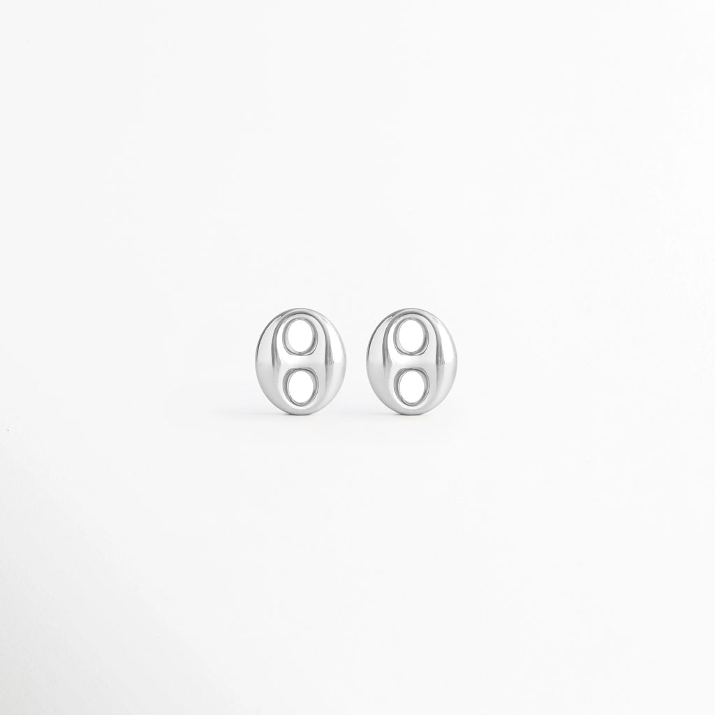 Aretes Sahra Silver Studs de acero inoxidable con recubrimiento en Oro Blanco 18K y diseño geométrico ovalado sobre fondo blanco, Vista frontal de los Aretes Sahra Silver Studs con acabado en Oro Blanco 18K y estilo minimalista, Aretes Sahra Silver Studs con diseño ovalado contemporáneo elaborados en acero inoxidable, Par de Aretes Sahra Silver Studs con acabado plateado brillante y diseño geométrico moderno, Aretes Sahra Silver Studs de acero inoxidable con diseño elegante y acabado en Oro Blanco 18K.