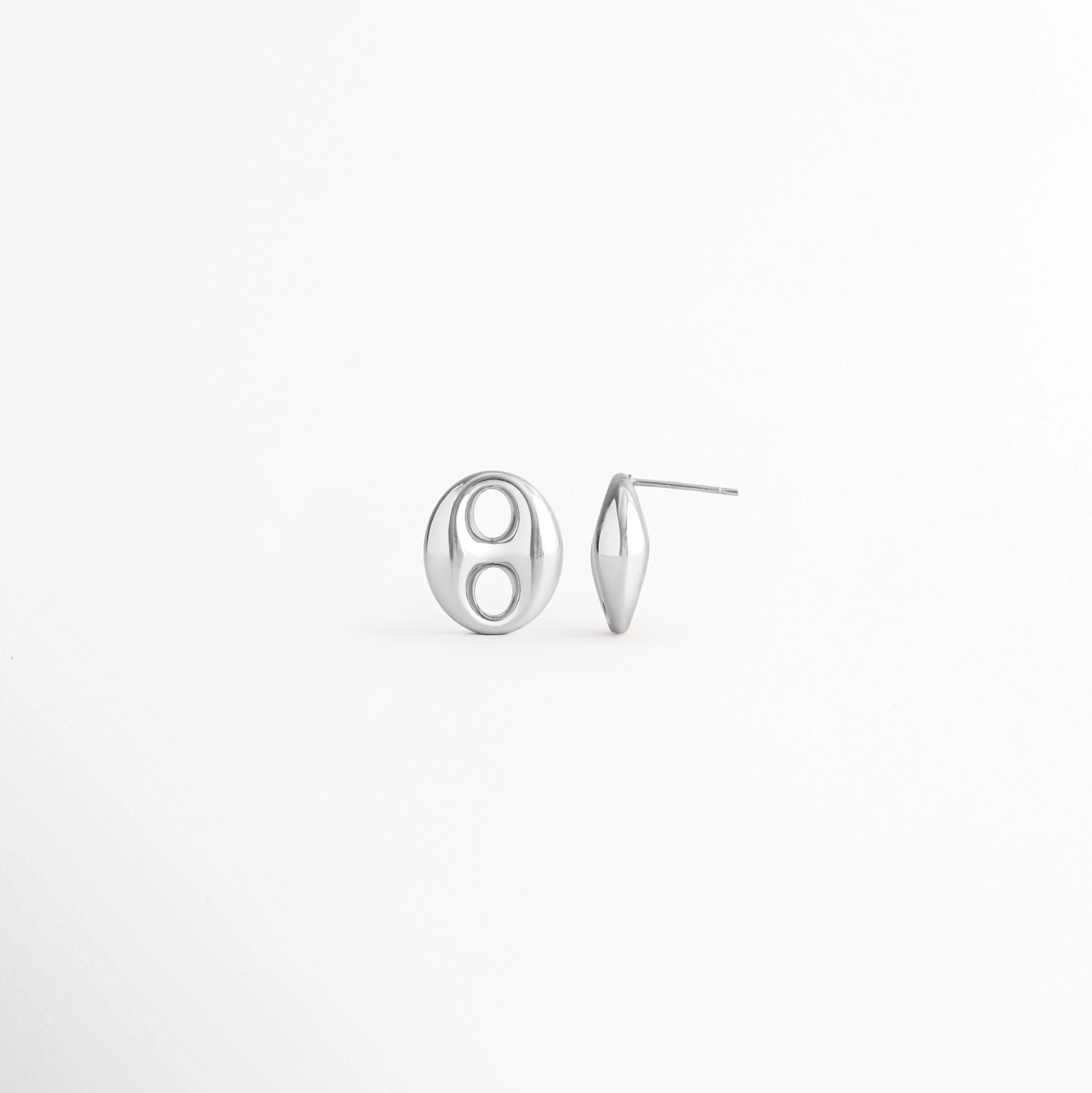 Vista en ángulo de los Aretes Sahra Silver Studs mostrando el perfil y el broche tipo poste, Perspectiva de los Aretes Sahra Silver Studs con acabado en Oro Blanco 18K y diseño geométrico, Aretes Sahra Silver Studs fotografiados de perfil resaltando su acabado plateado brillante, Vista diagonal de los Aretes Sahra Silver Studs elaborados en acero inoxidable con recubrimiento en Oro Blanco 18K, Aretes Sahra Silver Studs en perspectiva mostrando su estructura y diseño minimalista.
