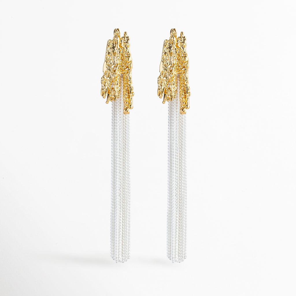 Aretes Grutas de diseño largo bitono con cabezal dorado de textura rocosa orgánicamente esculpida y flecos de cadenas finas en tono plata, Vista frontal de aretes largos de 8.7 cm enchapados en oro y oro blanco 18K con remate rugoso de inspiración mineral y cascada de cadenas, Plano general de par de aretes colgantes dramáticos de copper con topes dorados texturizados y fleco de cadenas plateadas sobre fondo blanco, Aretes Grutas destacando la combinación de texturas 
