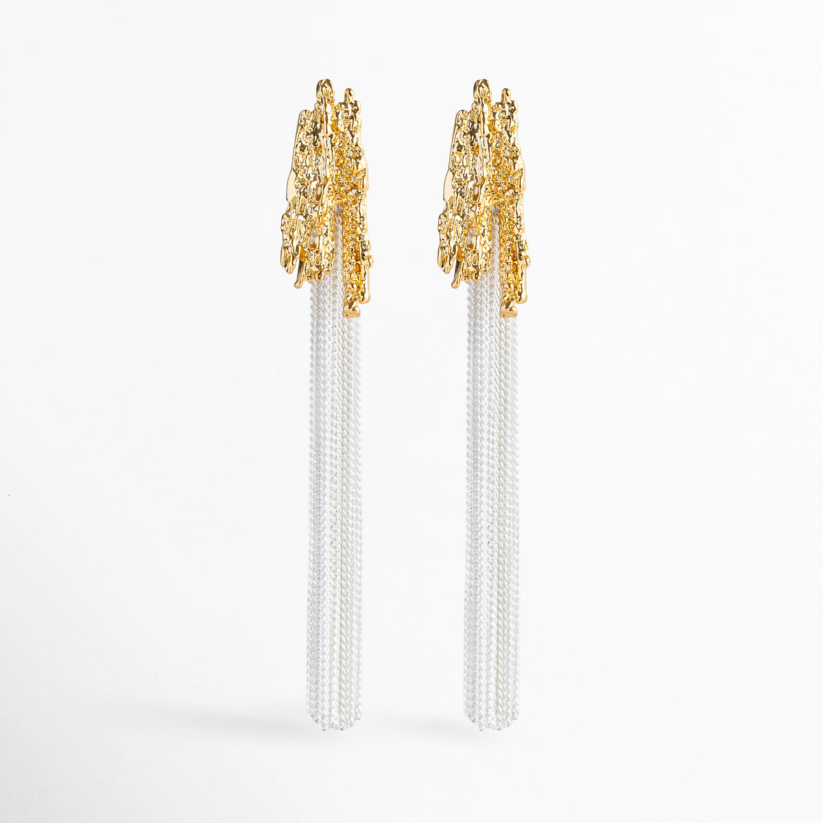 Aretes Grutas de diseño largo bitono con cabezal dorado de textura rocosa orgánicamente esculpida y flecos de cadenas finas en tono plata, Vista frontal de aretes largos de 8.7 cm enchapados en oro y oro blanco 18K con remate rugoso de inspiración mineral y cascada de cadenas, Plano general de par de aretes colgantes dramáticos de copper con topes dorados texturizados y fleco de cadenas plateadas sobre fondo blanco, Aretes Grutas destacando la combinación de texturas 