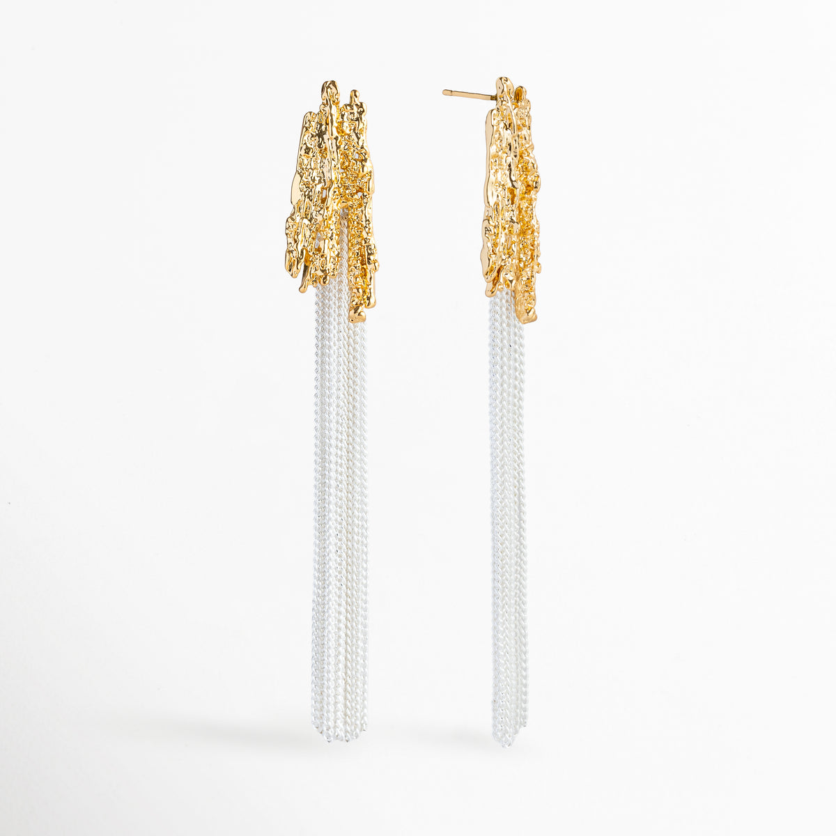 Vista de perfil de los Aretes Grutas mostrando el poste de sujeción para oreja perforada y la textura tridimensional del tope dorado, Acercamiento lateral a los aretes colgantes resaltando la estructura rocosa enchapada en oro 18K y la caída vertical de las cadenas, Toma en ángulo que muestra la profundidad y el volumen de la textura escultural inspirada en las estalactitas de cueva, Muestra de la proporción de 8.7 cm de largo de los aretes y el acabado pulido bitono.