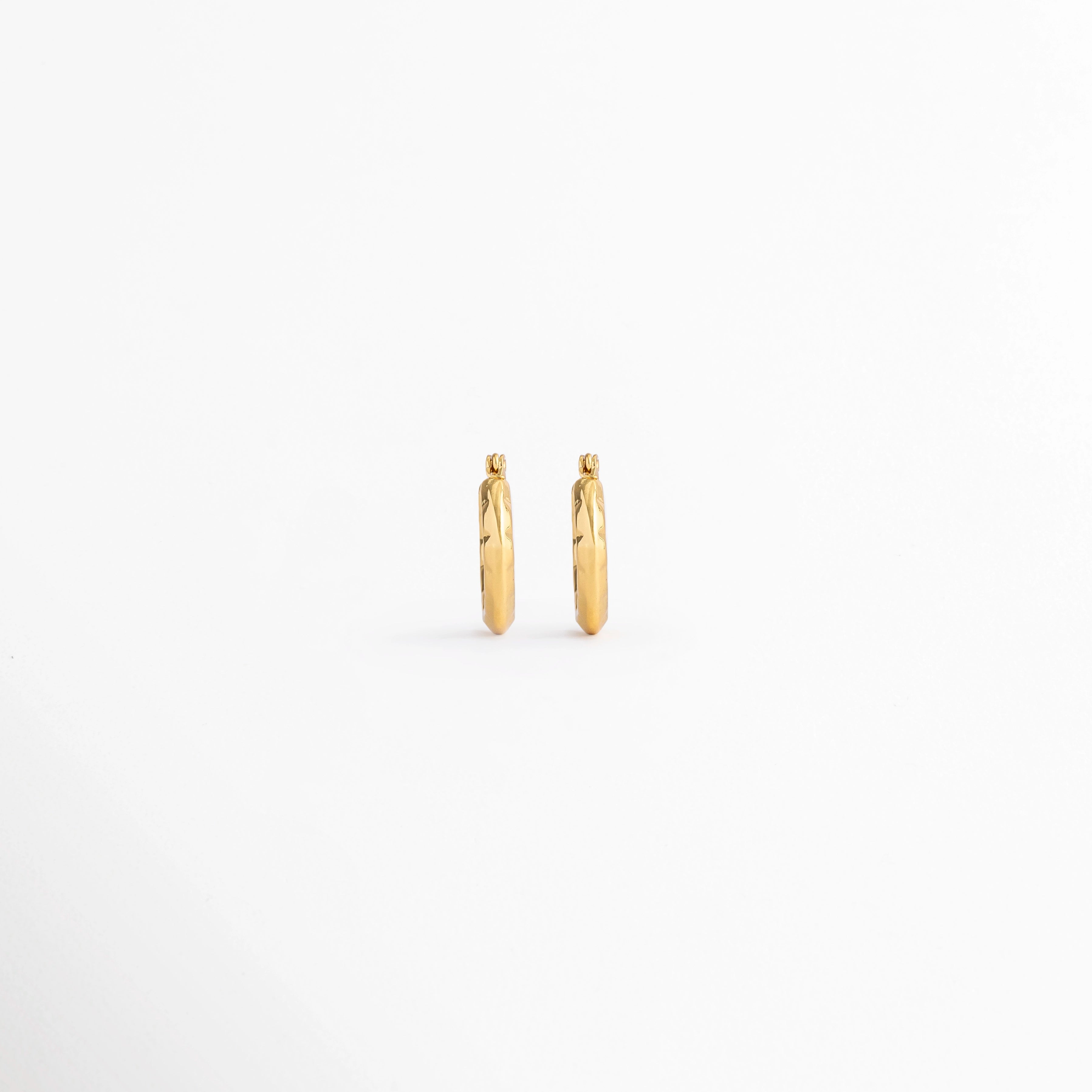 Vista posterior de los Aretes Doré Hoops mostrando el cierre tipo bisagra y el acabado en Oro 18K, Parte trasera de los Aretes Doré Hoops con sistema de cierre tipo huggie y acabado dorado, Aretes Doré Hoops en vista posterior destacando la estructura del aro y el mecanismo de cierre, Detalle de la parte posterior de los Aretes Doré Hoops elaborados en acero inoxidable, Vista trasera de los Aretes Doré Hoops con diseño clásico y cierre seguro.