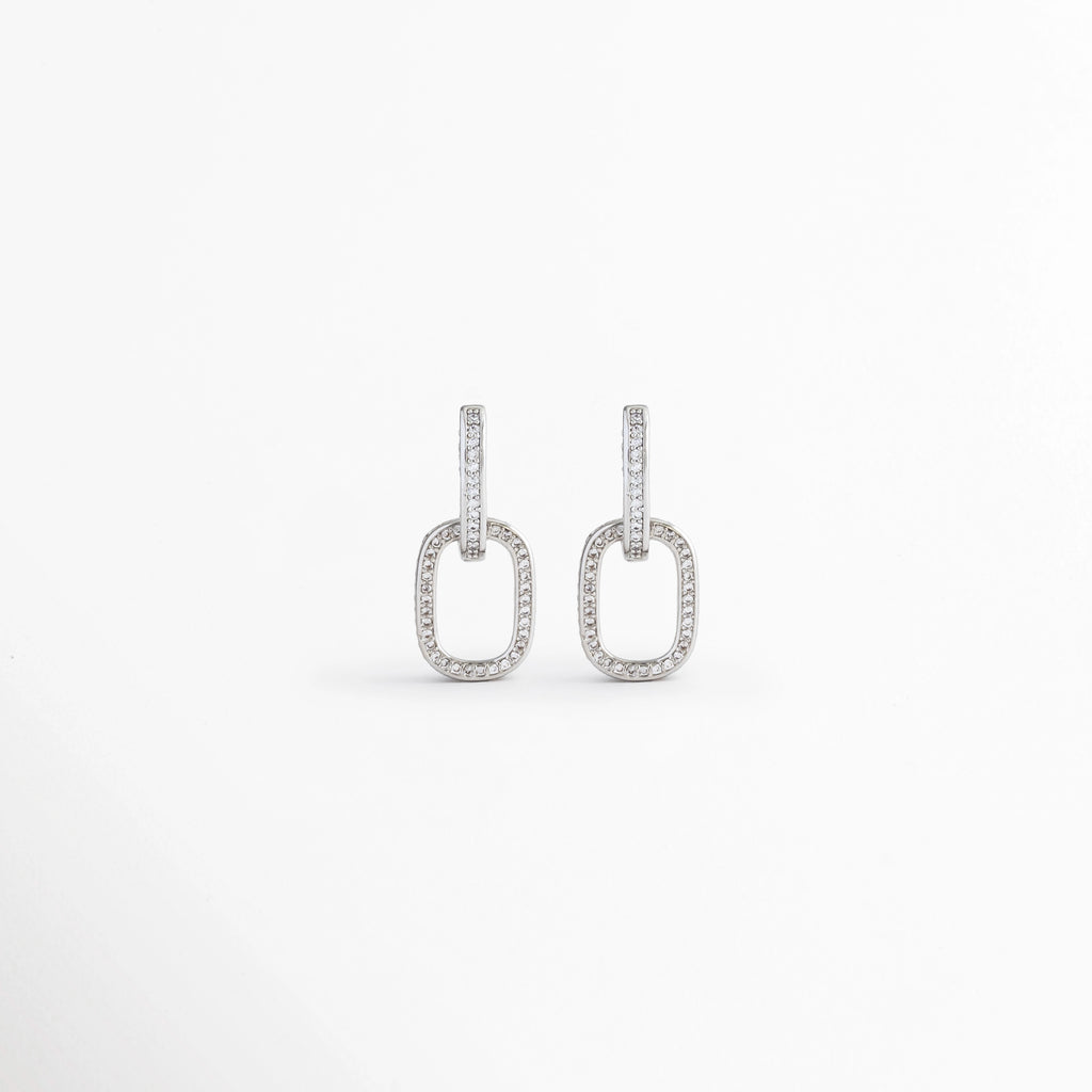 Aretes Silver Oria de cobre con recubrimiento en Oro Blanco 14K e incrustación de zirconia sobre fondo blanco, Vista frontal de los Aretes Silver Oria con diseño rectangular y zirconia en acabado de Oro Blanco 14K, Aretes Silver Oria con diseño geométrico de eslabón rectangular y zirconia brillante, Par de Aretes Silver Oria con acabado plateado y diseño minimalista para mujer, Aretes Silver Oria con forma rectangular y acabado en Oro Blanco 14K.