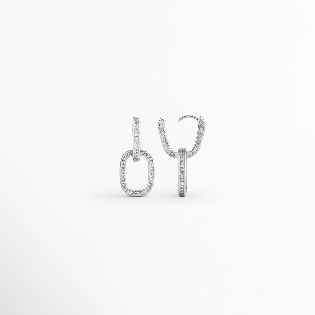 Vista lateral de los Aretes Silver Oria mostrando el perfil del diseño rectangular y el broche, Perfil de los Aretes Silver Oria con acabado en Oro Blanco 14K y zirconia incrustada, Aretes Silver Oria en vista lateral destacando el grosor de la pieza y el sistema de cierre, Detalle lateral de los Aretes Silver Oria elaborados en cobre con recubrimiento en Oro Blanco 14K, Vista de costado de los Aretes Silver Oria con diseño geométrico elegante y zirconia.