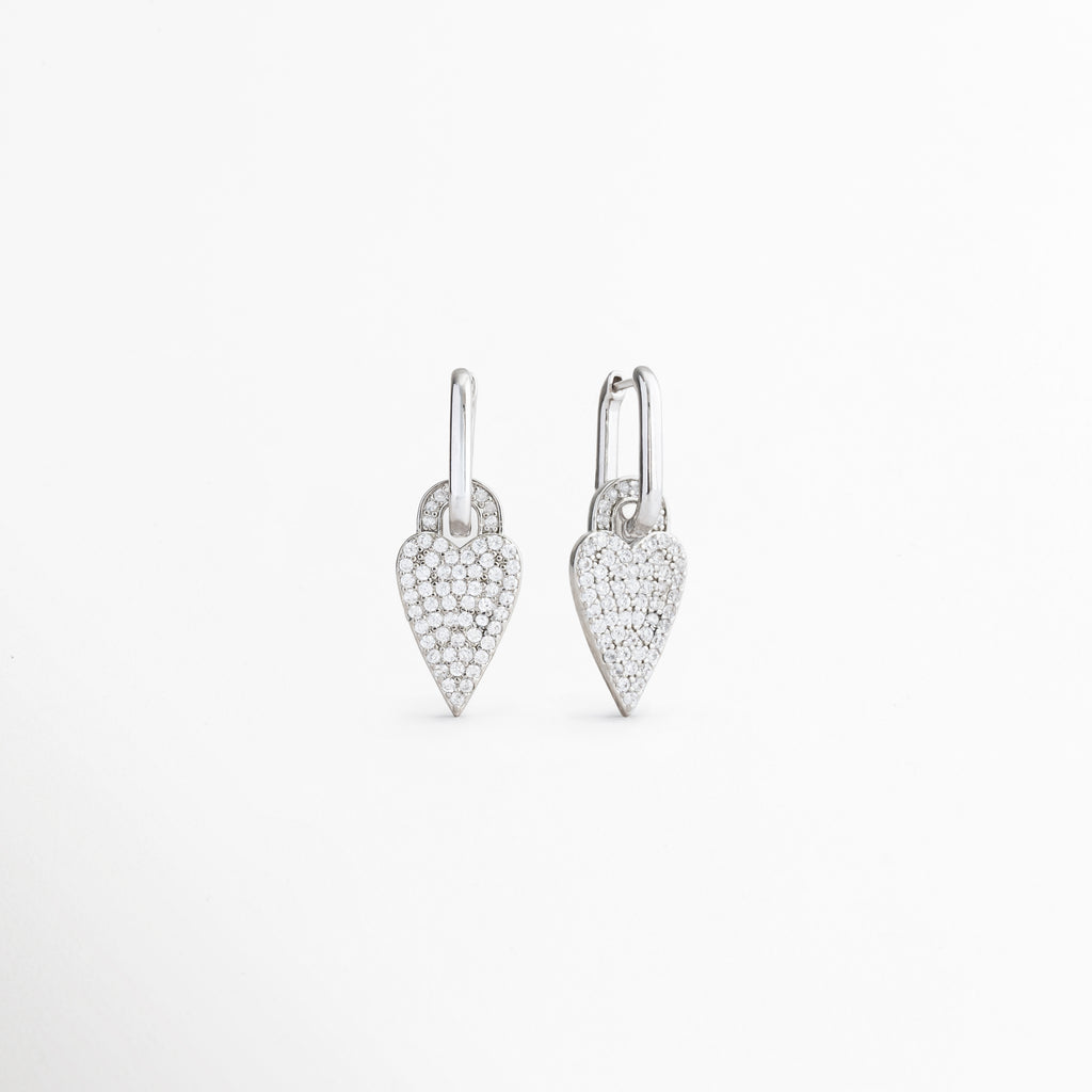 Vista lateral de aretes Silver Velvet Hoops con corazón, Perfil de pendientes plateados con charm de zirconias, Detalle lateral de aretes tipo aro con dije de corazón, Aretes con acabado brillante y diseño delicado, Vista lateral de pendientes con corazón colgante.