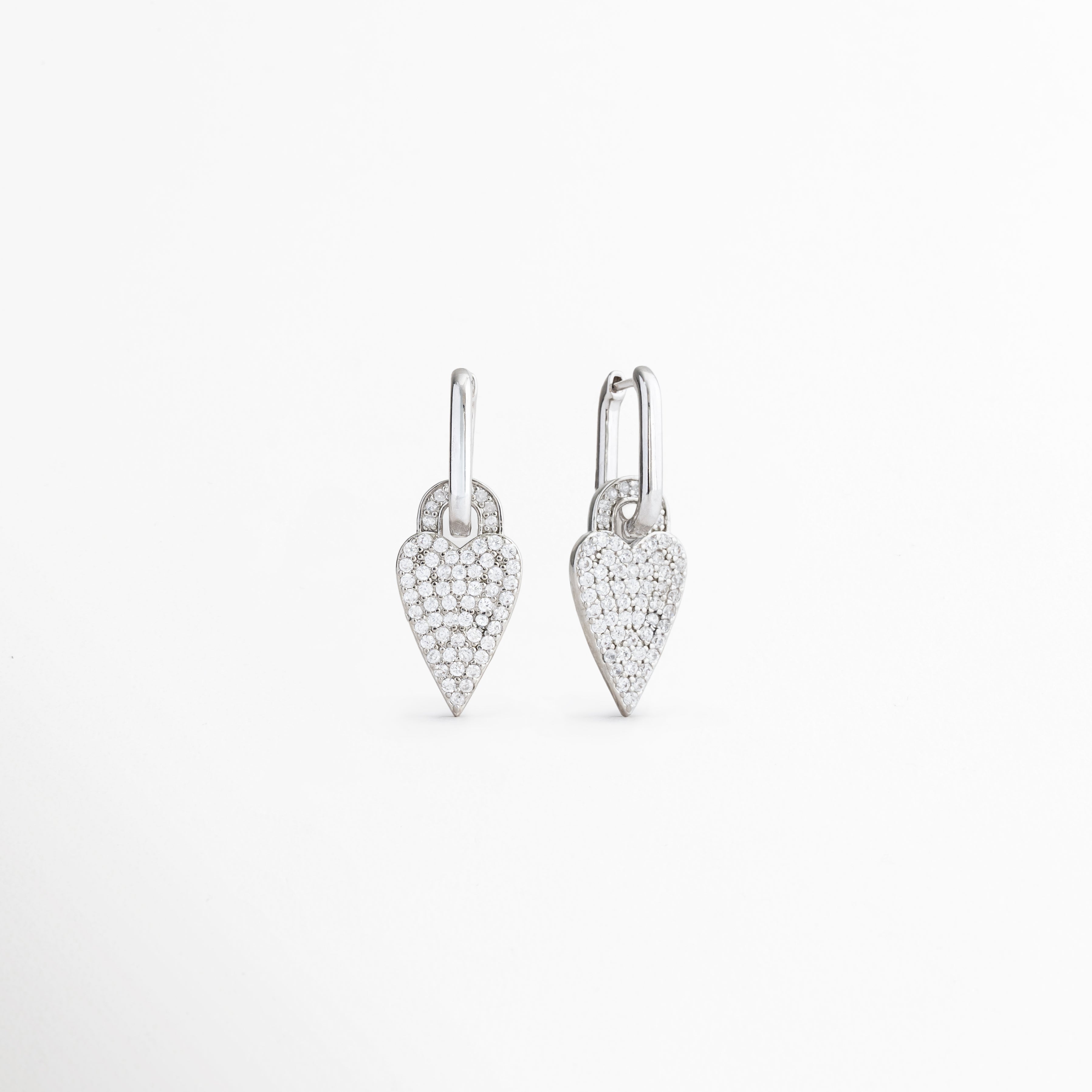 Vista lateral de aretes Silver Velvet Hoops con corazón, Perfil de pendientes plateados con charm de zirconias, Detalle lateral de aretes tipo aro con dije de corazón, Aretes con acabado brillante y diseño delicado, Vista lateral de pendientes con corazón colgante.